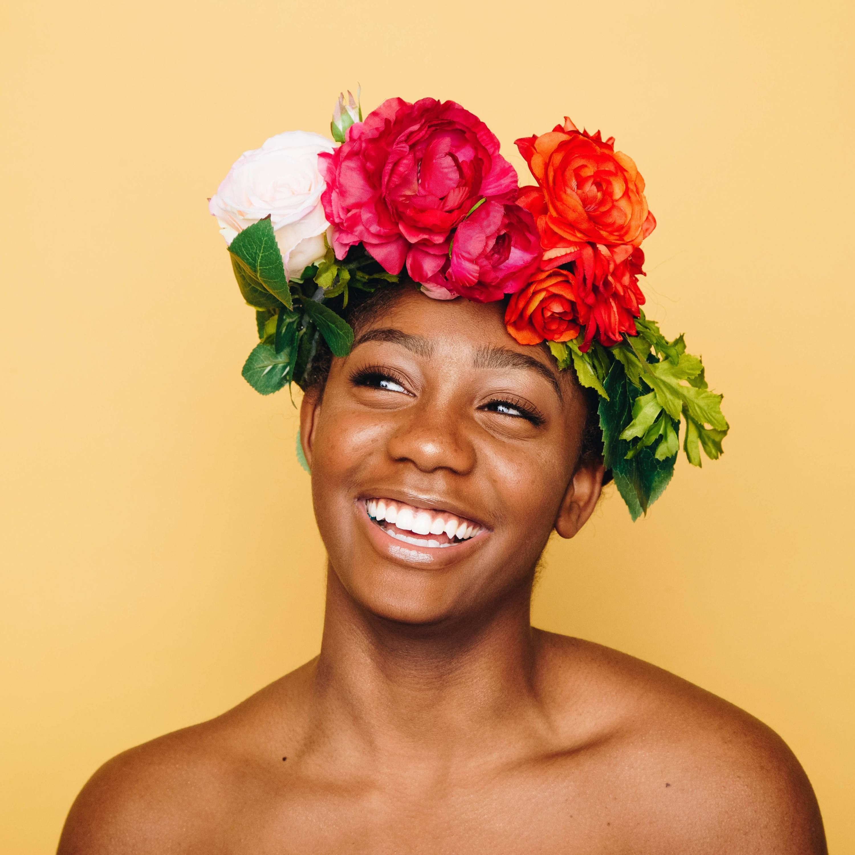Smiling person wearing colorful flower crown against yellow background