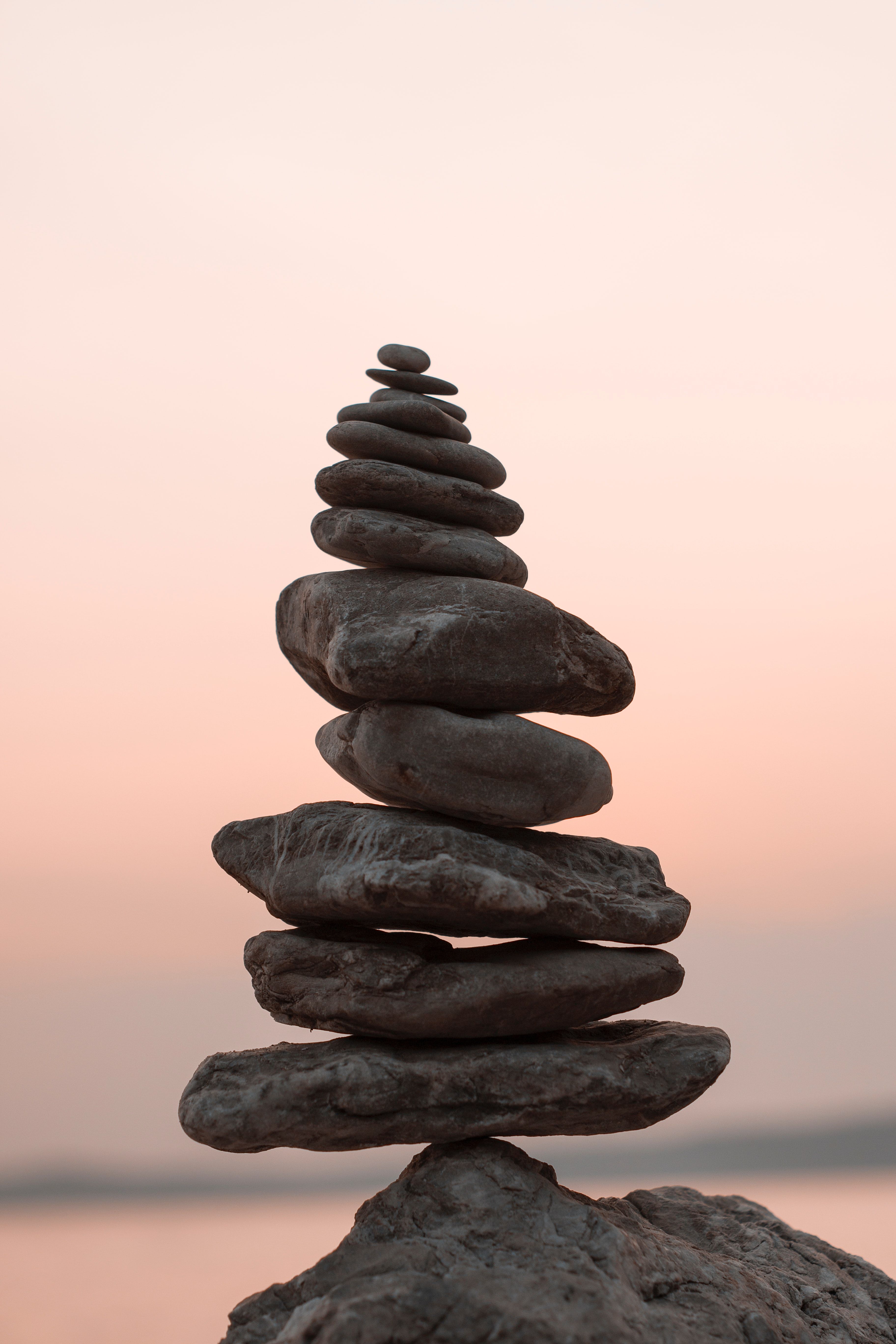 Balanced stack of dark rocks towers against a soft pink sunset sky