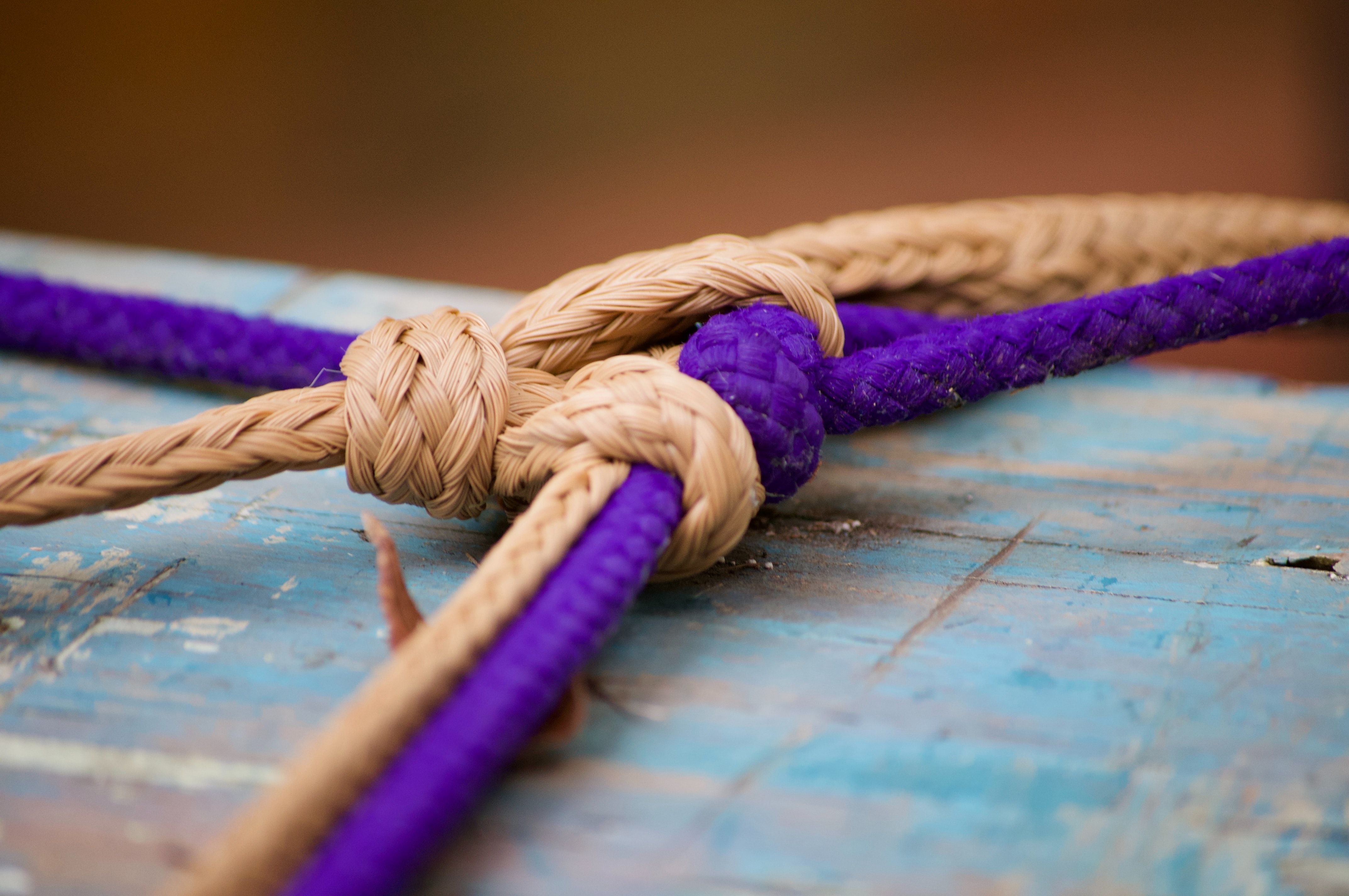 Braided ropes in beige and purple tied in knots on a weathered blue wooden surface.