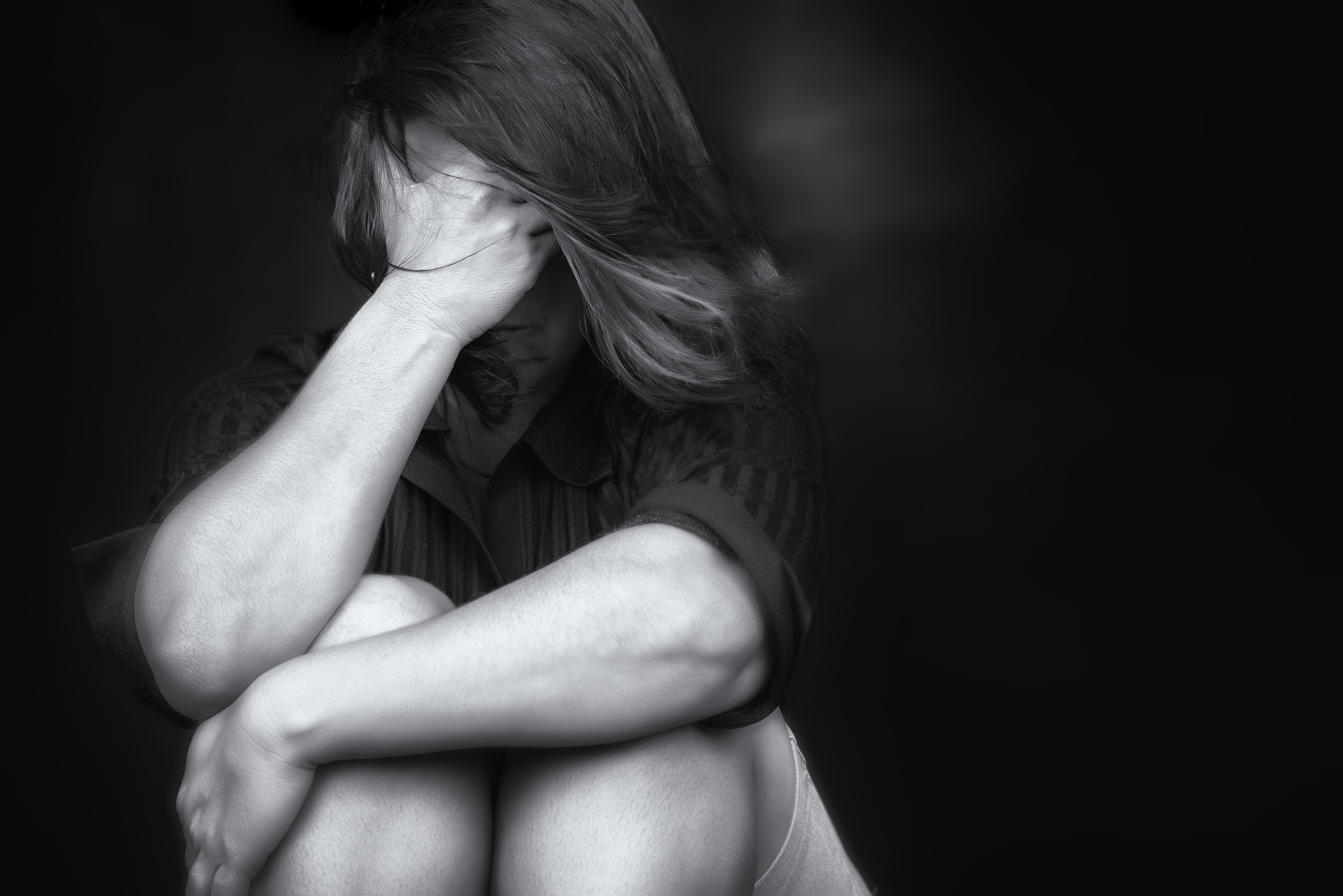 Black and white portrait of woman with head down, hand to face, expressing sadness or distress.
