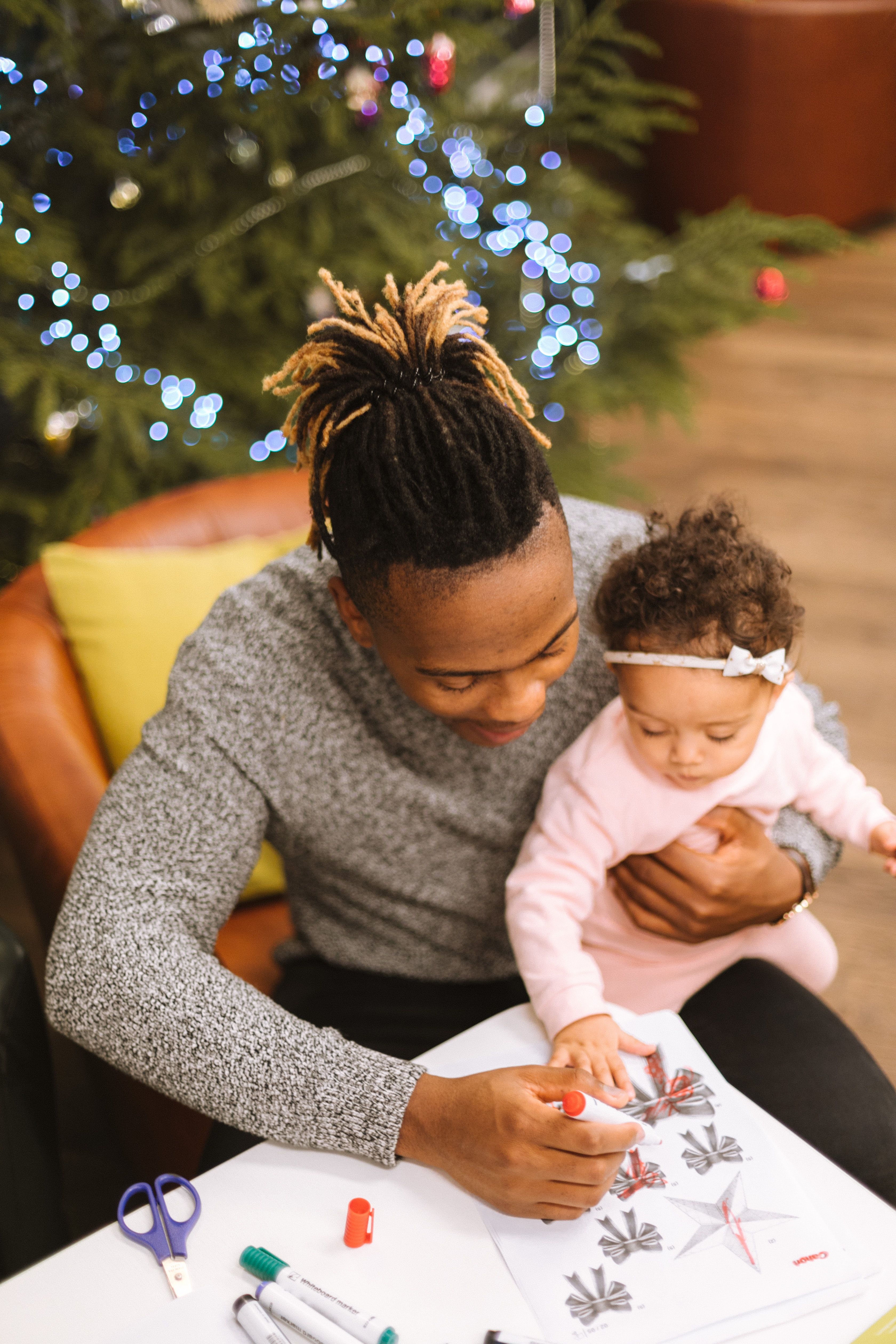 Woman and baby crafting together under decorated Christmas tree with blue lights