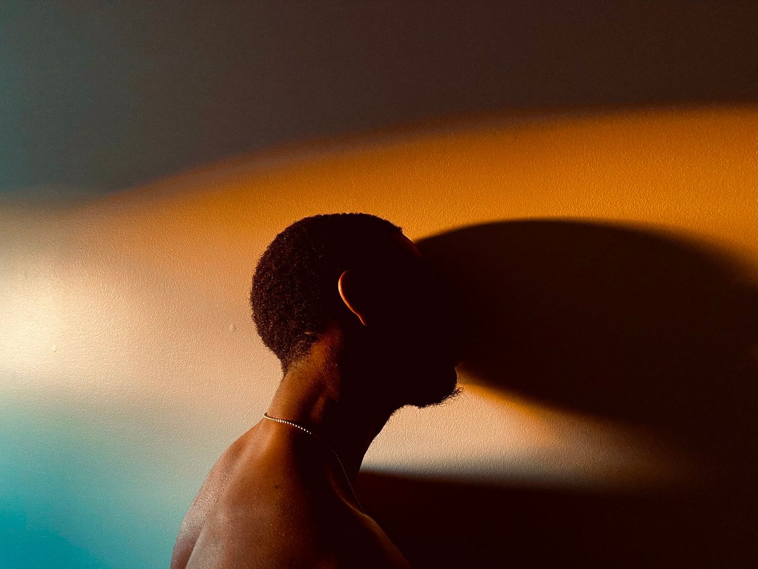 Silhouetted person in profile with dramatic orange and blue lighting, wearing beaded bracelet.