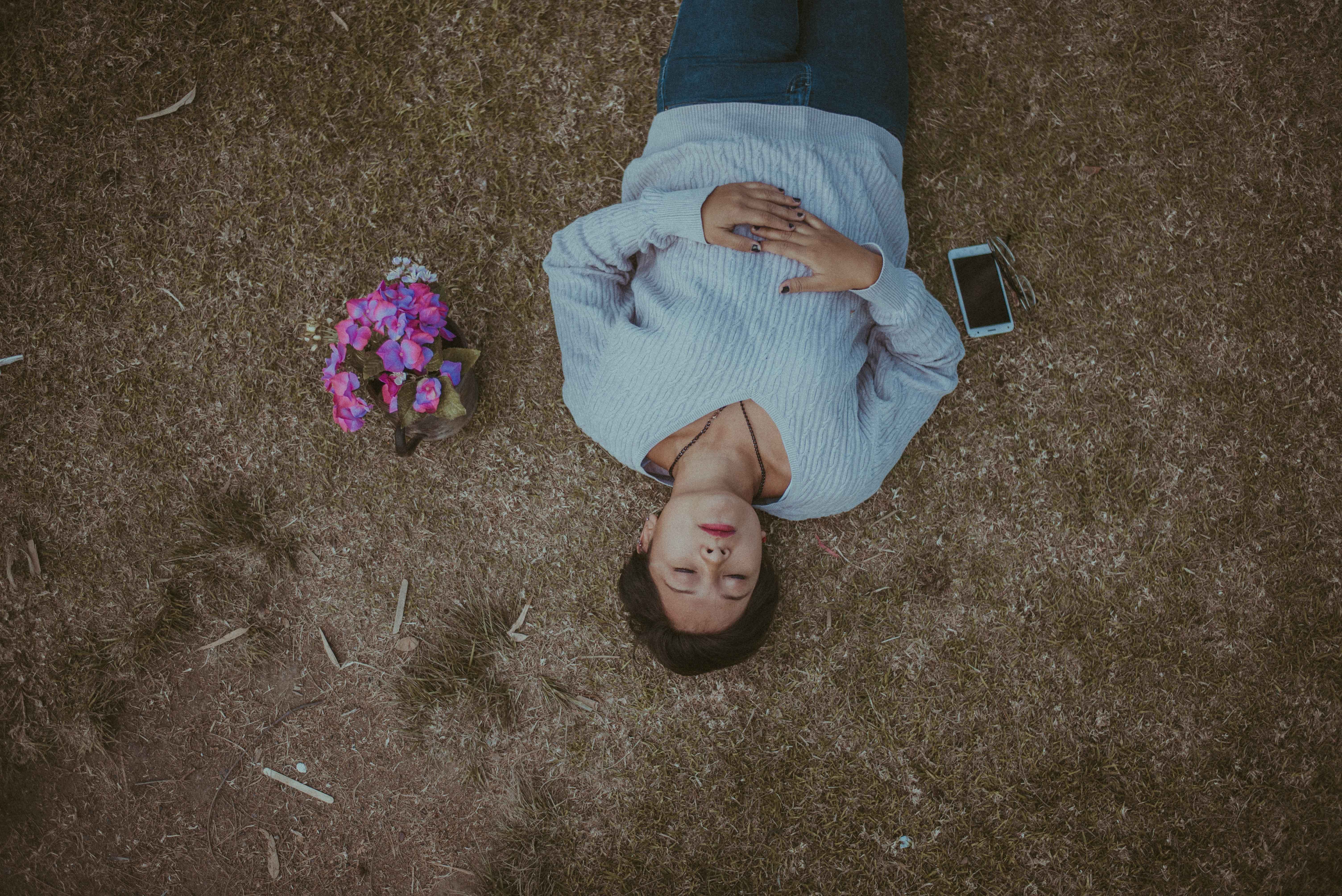 Woman lying on ground holding pink flowers with smartphone nearby, overhead view