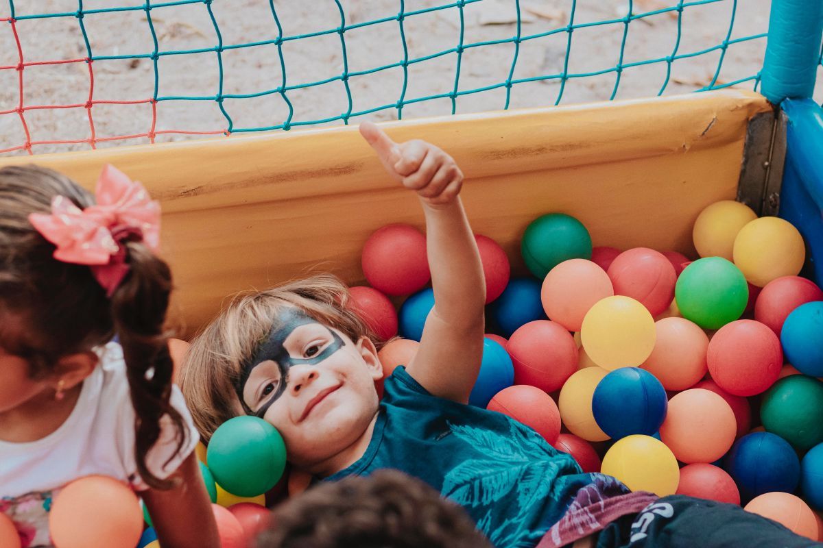 Child with face paint playing in colorful ball pit surrounded by nets