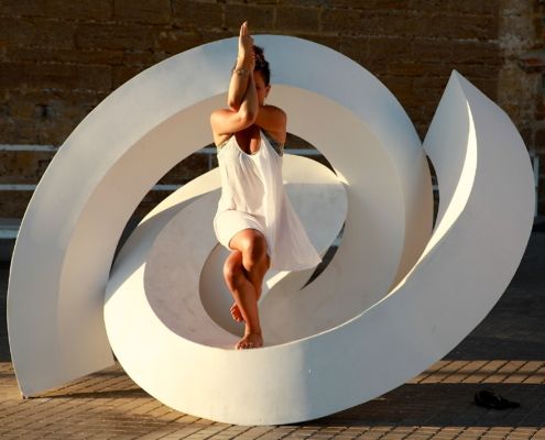 Dancer in white cloth posing gracefully within large white spiral sculpture