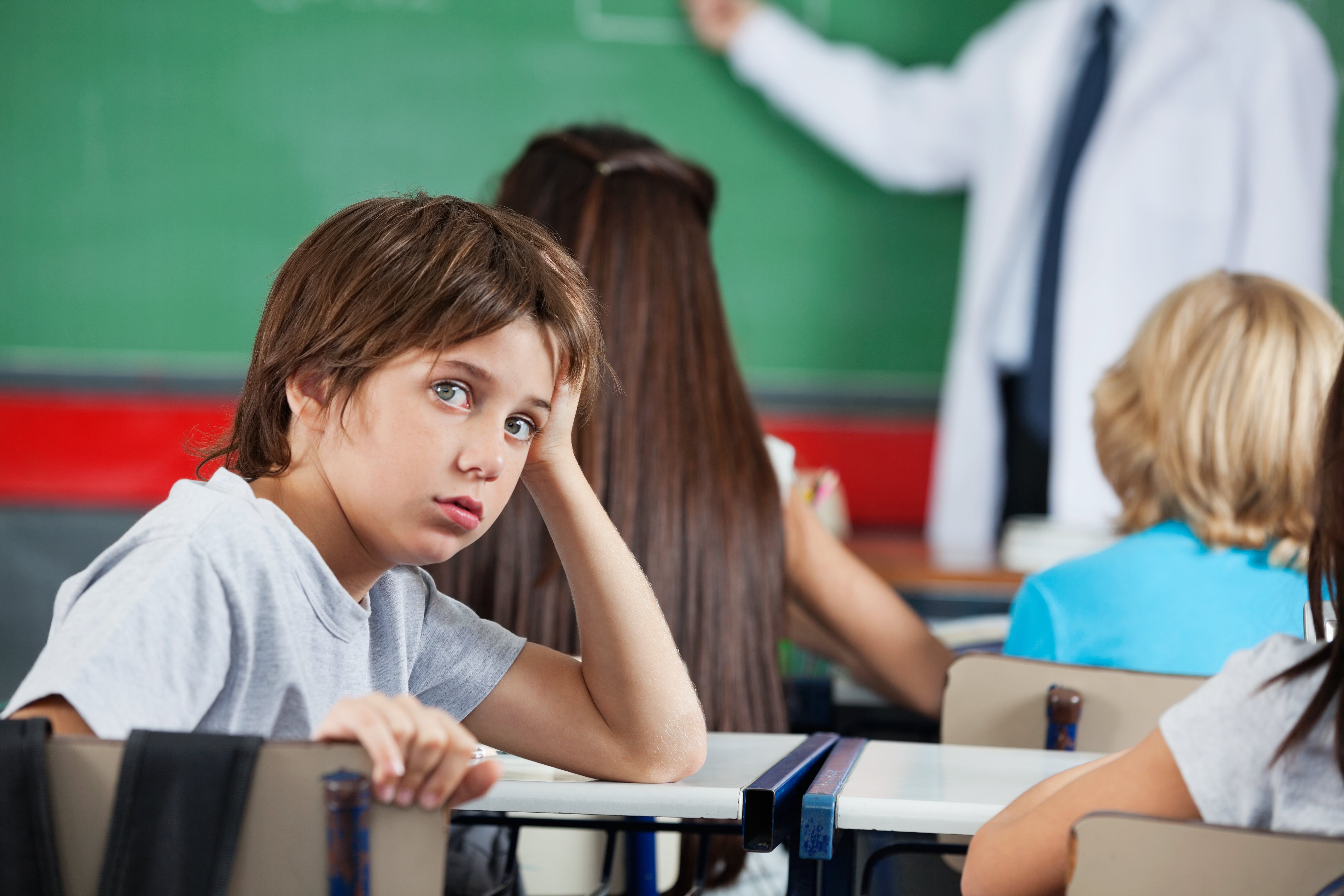 Bored student with hand on face during class at school desk