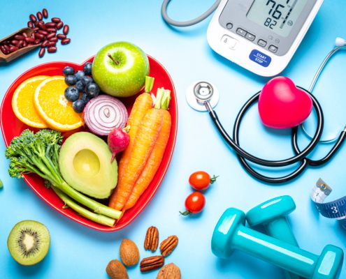 Heart-shaped red plate with healthy foods, blood pressure monitor, stethoscope, and dumbbells on blue background