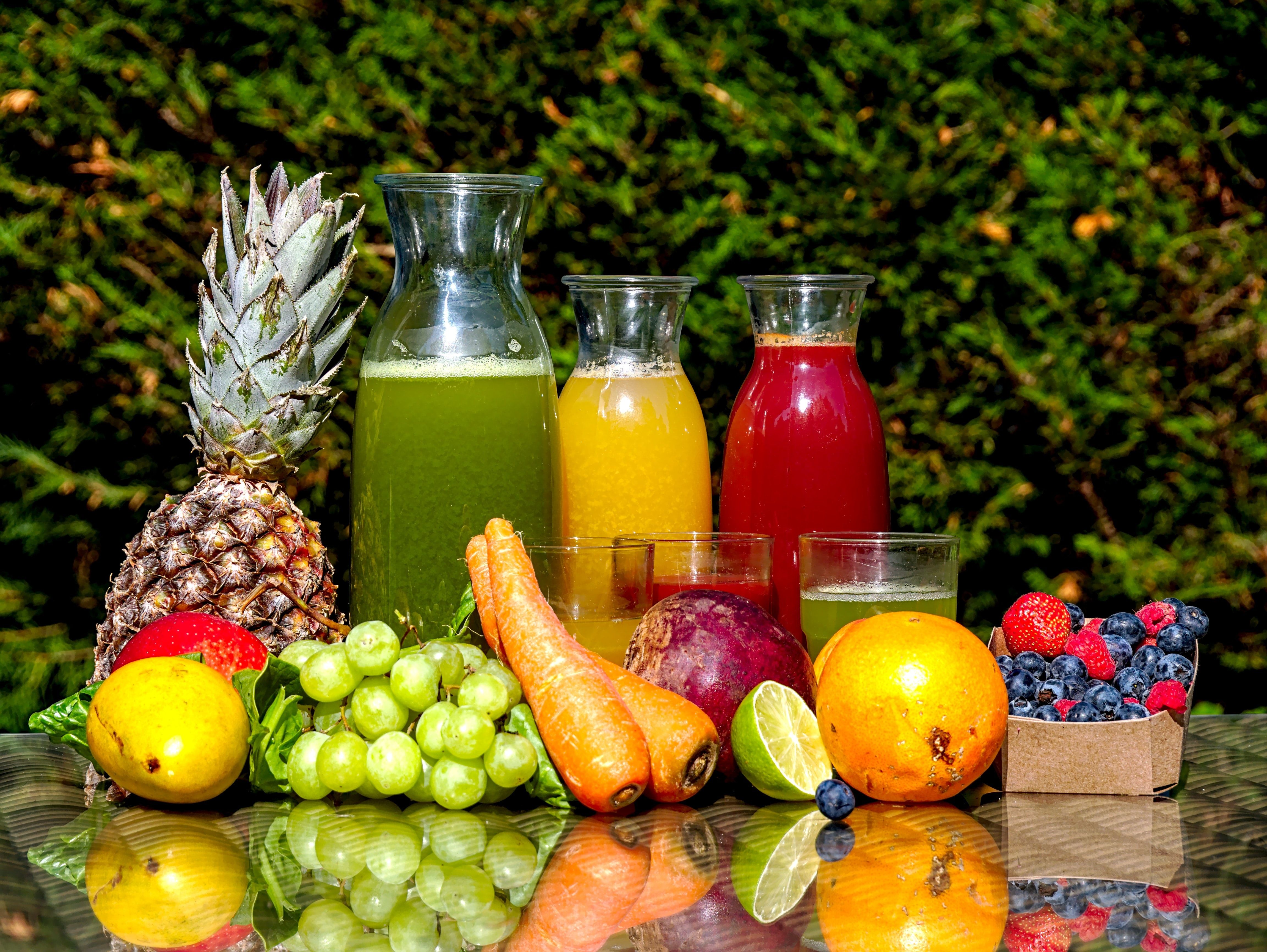 Fresh fruits and colorful juices displayed with pineapple, grapes, carrots, berries against green hedge