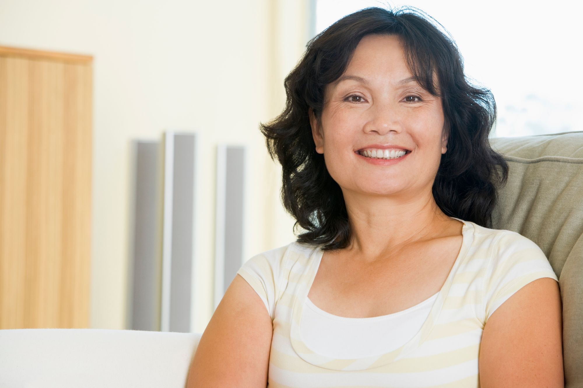 Middle-aged woman with black wavy hair smiling warmly indoors on couch