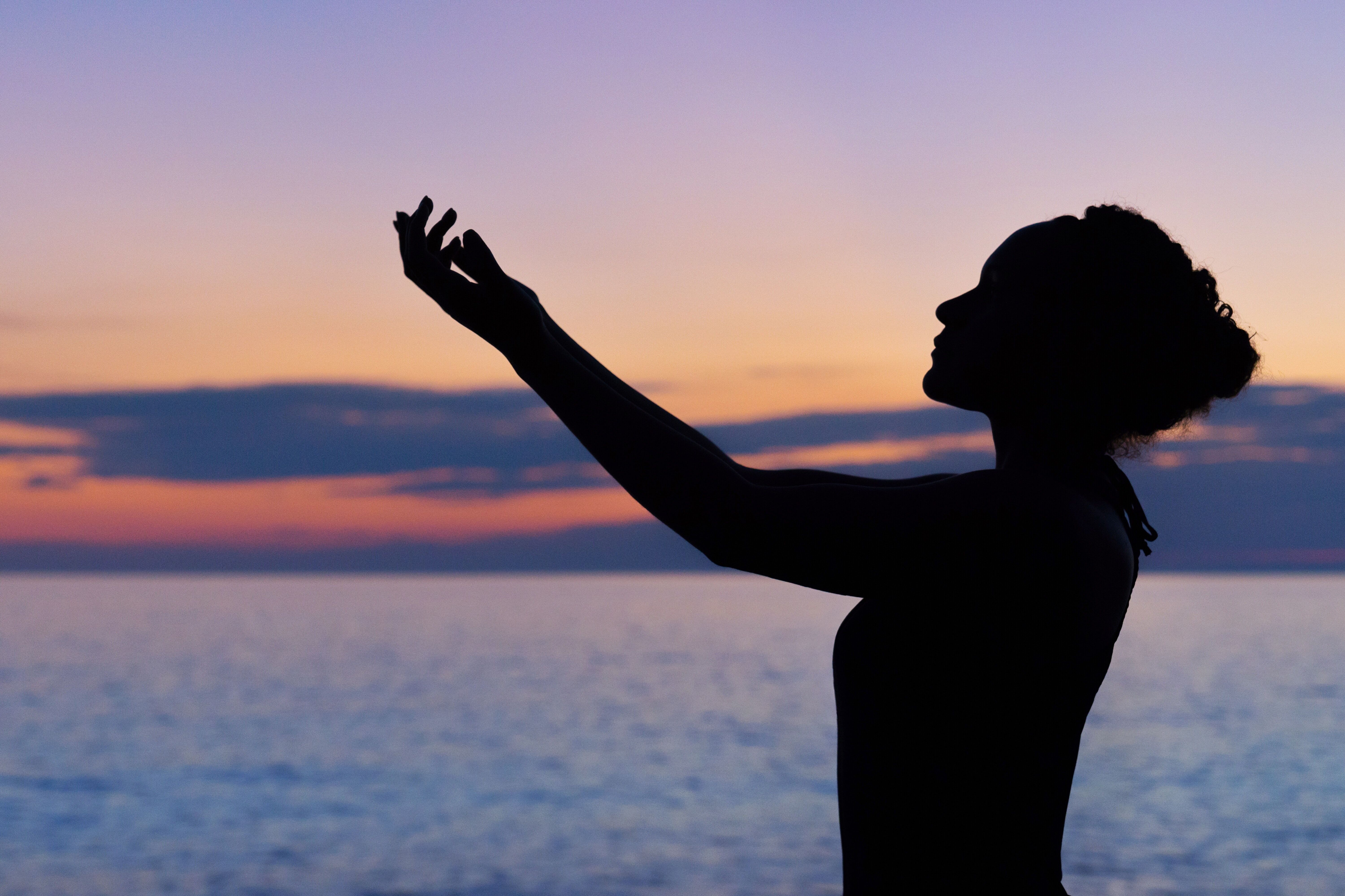 Silhouette of person with arm raised against colorful sunset over ocean