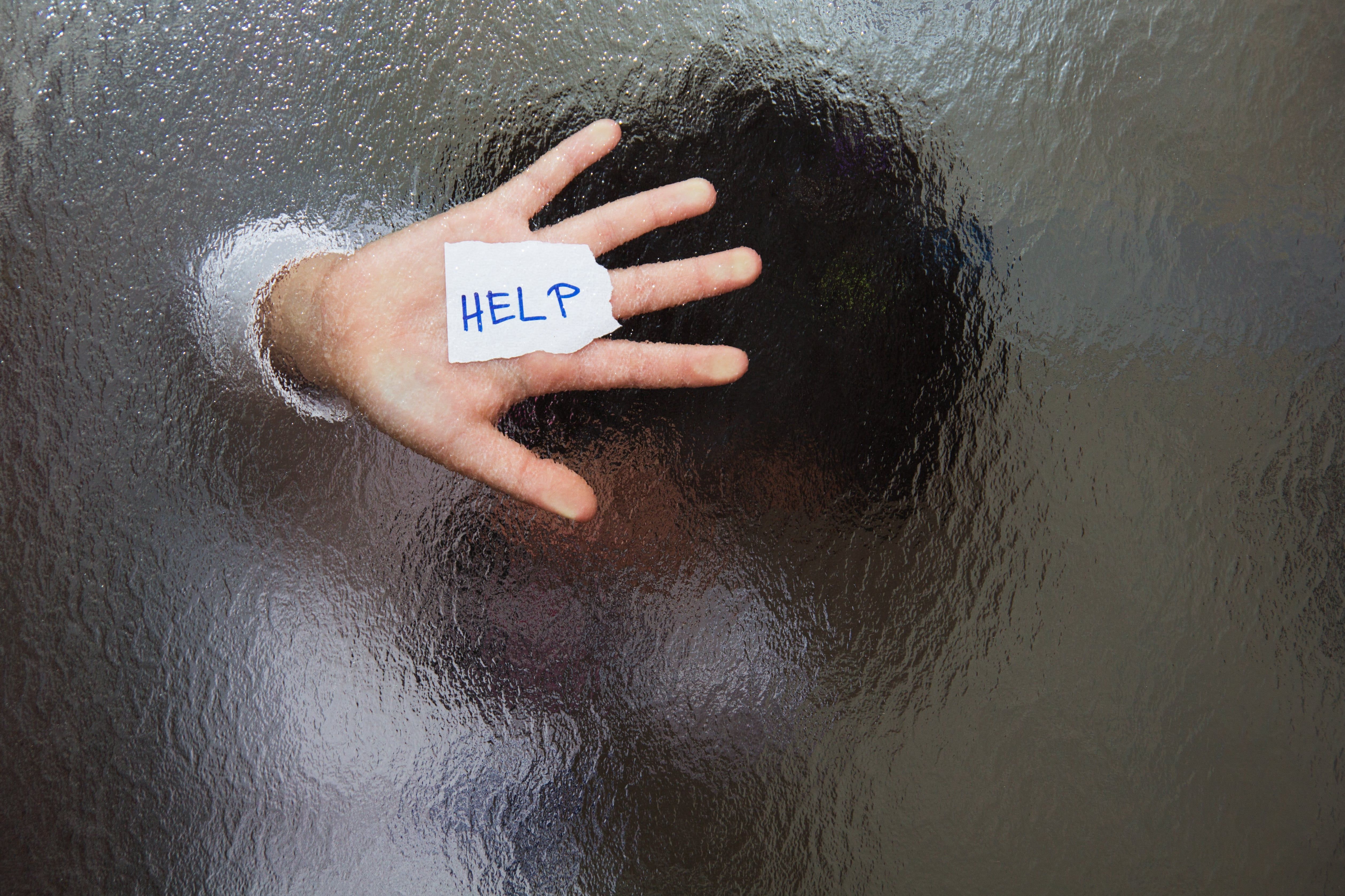 Person submerged in water with hand showing HELP sign written on palm