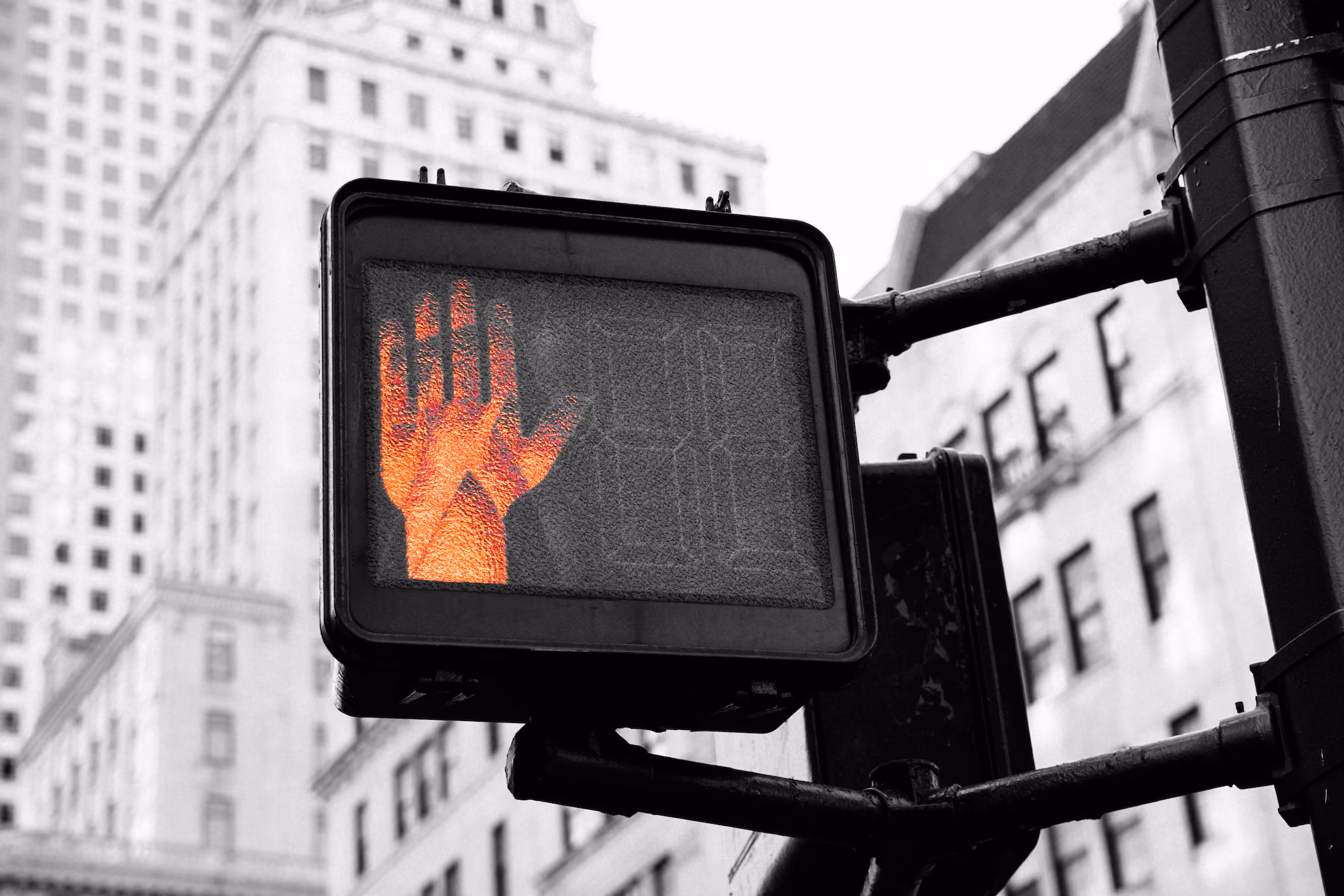 Traffic signal displaying open hand in orange against urban cityscape background