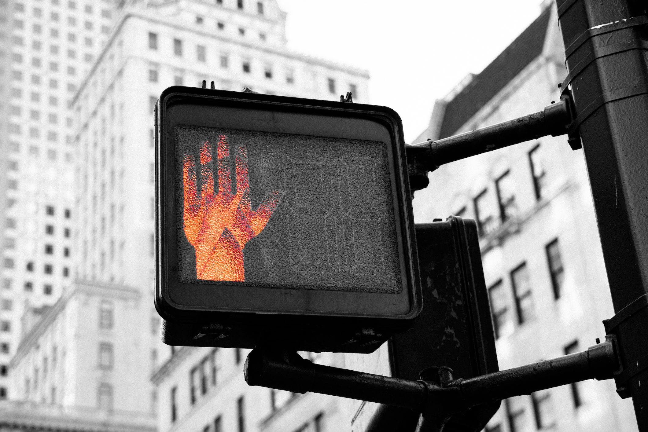 Traffic signal displaying open hand in orange against urban cityscape background