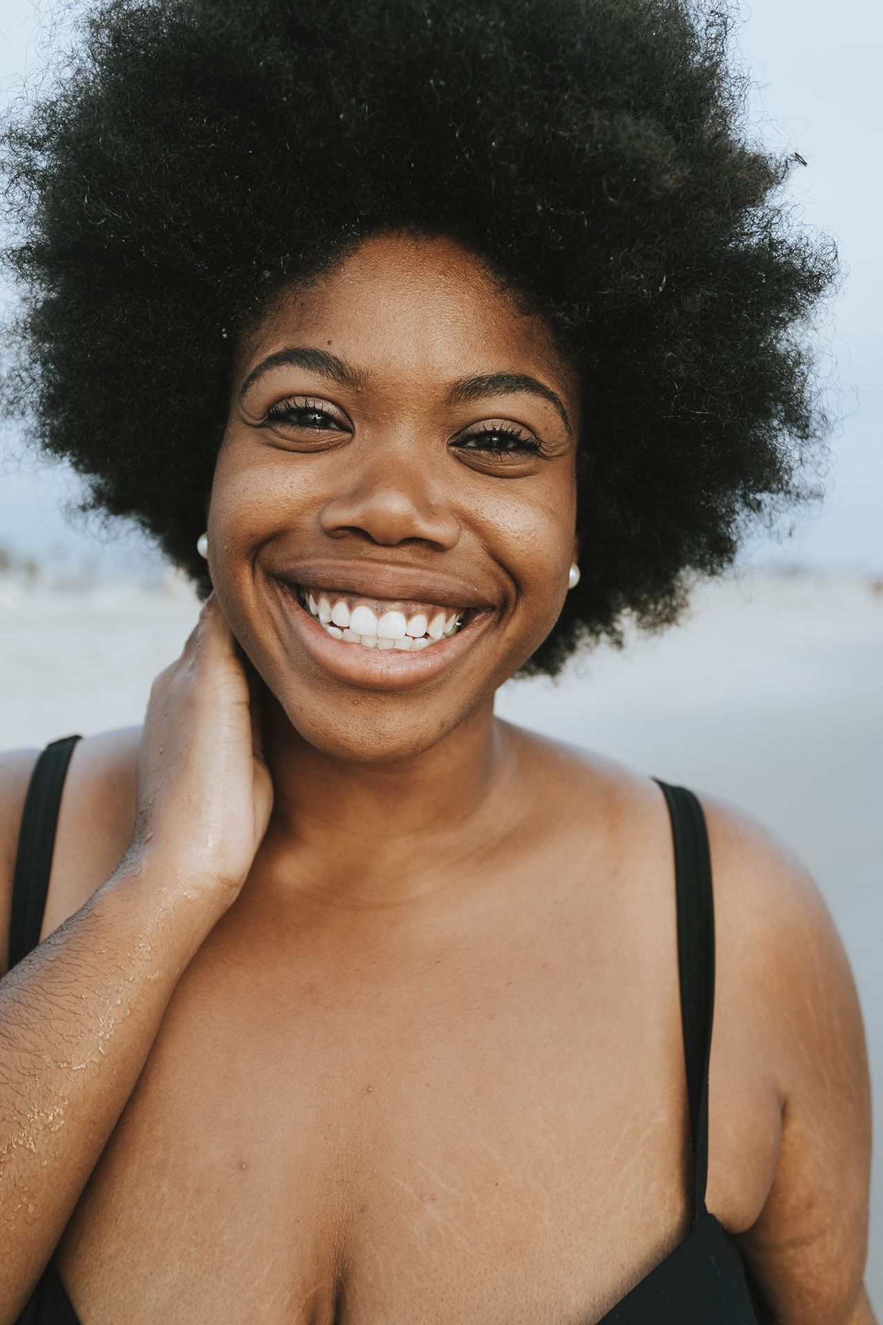 Portrait of smiling woman with natural black afro hair and hand to face