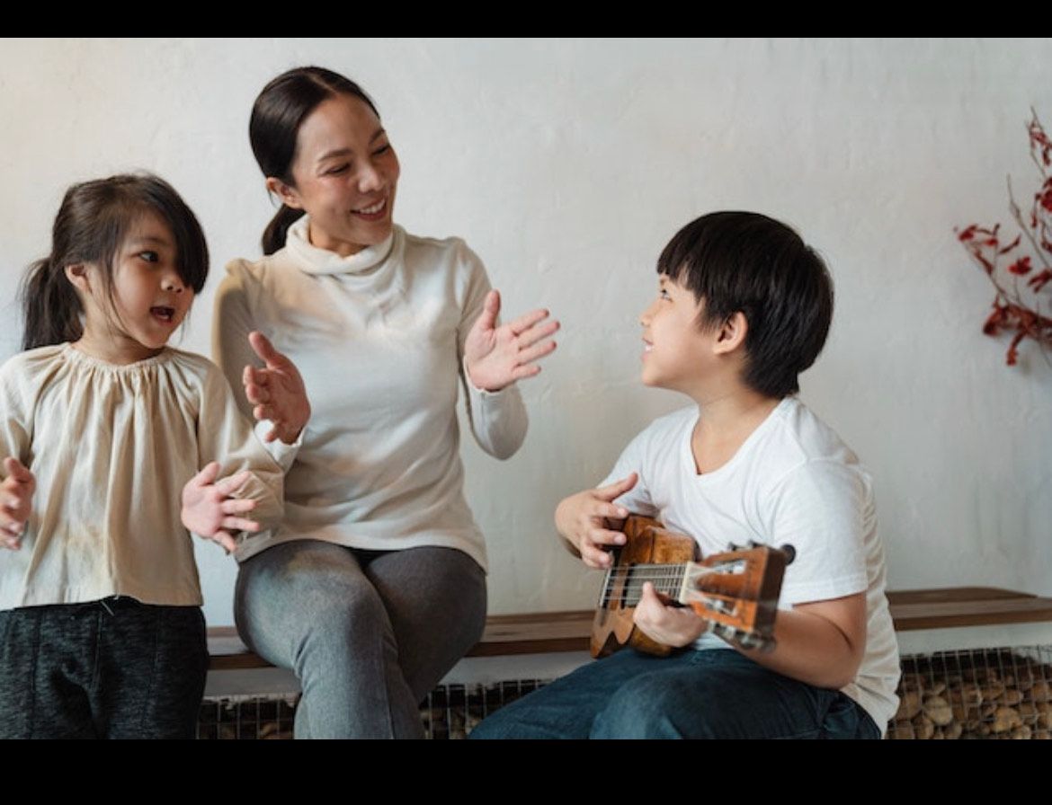Woman teaching two children to play guitar and sing together indoors