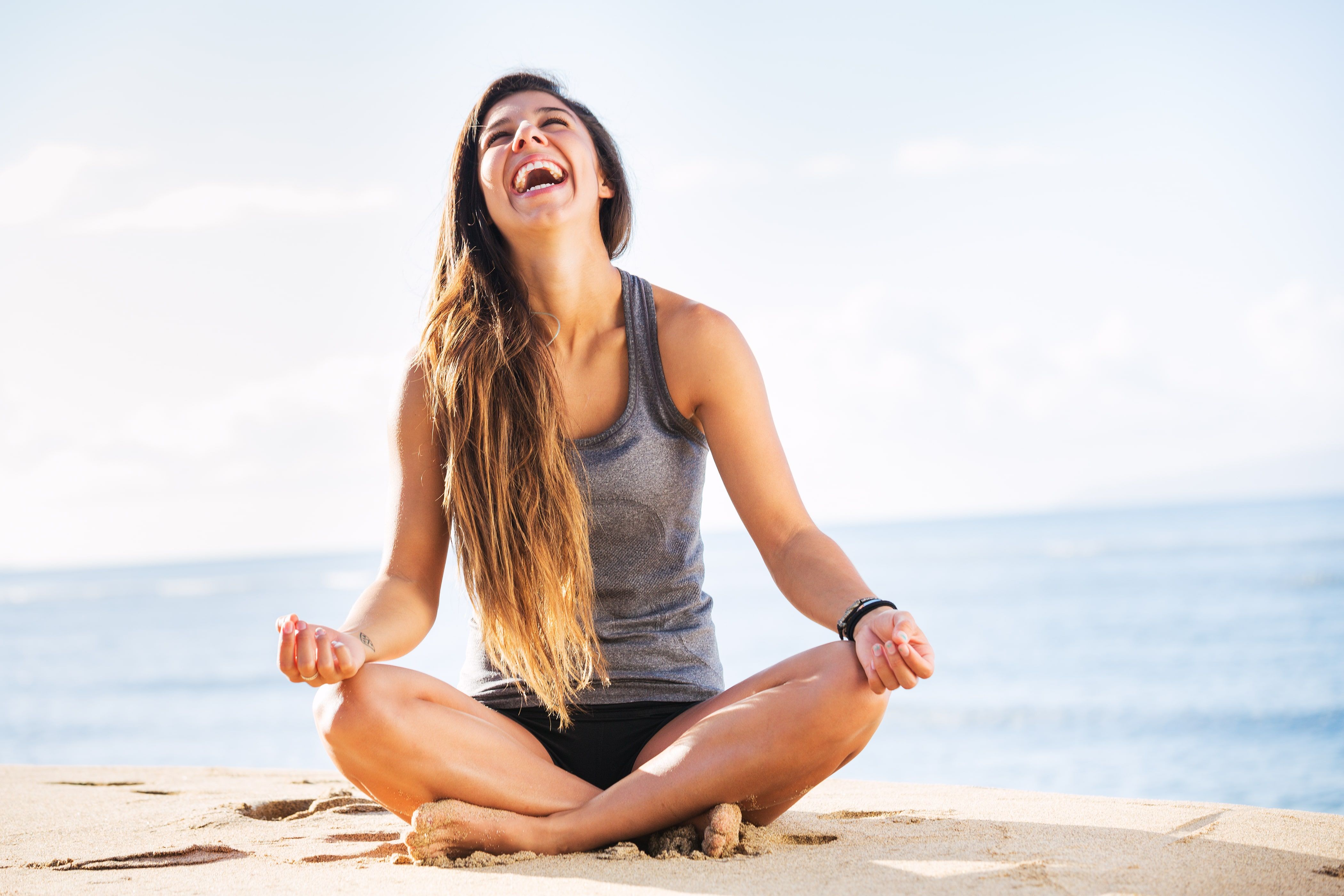 Happy woman meditating in lotus pose on beach with ocean background