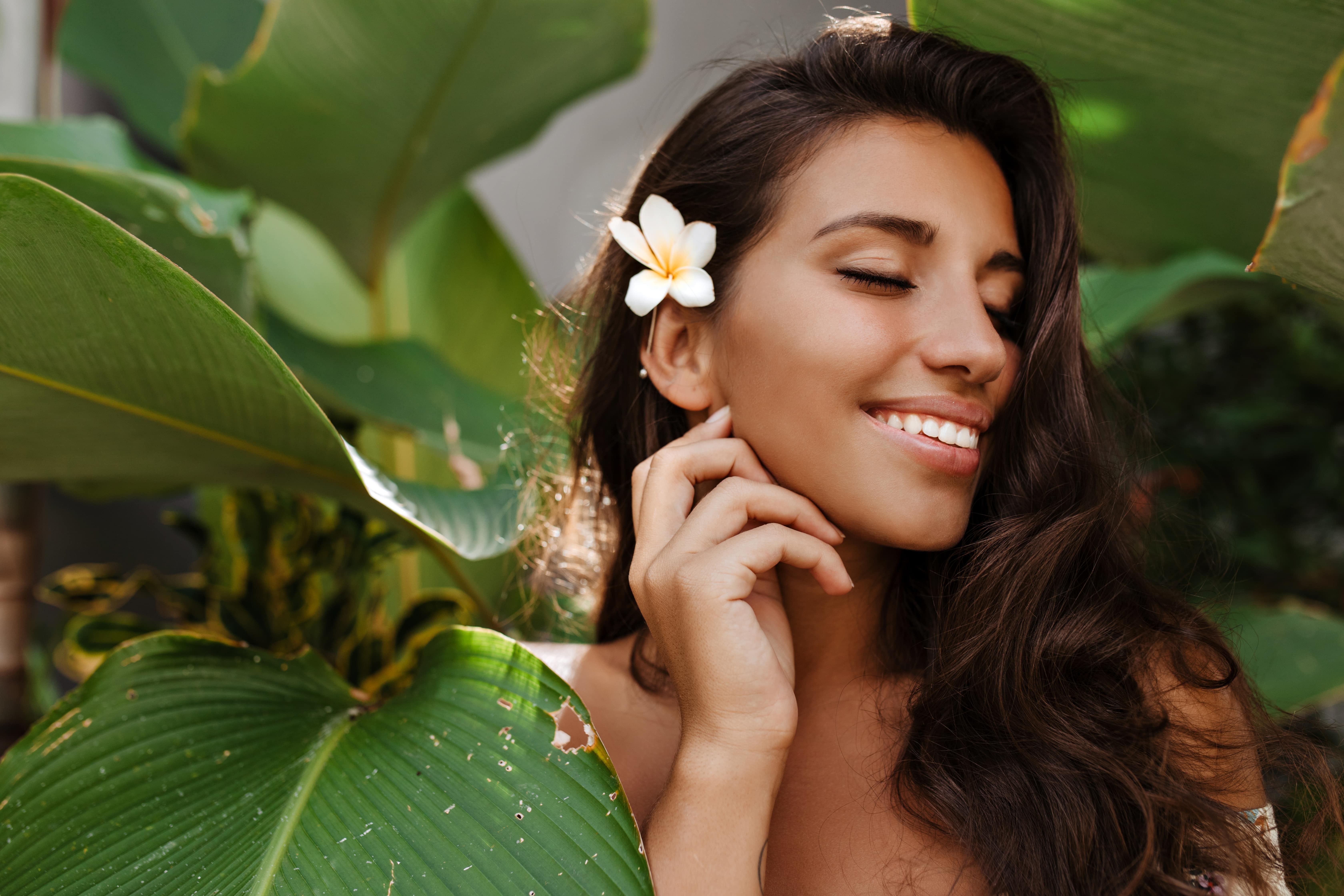 Woman with white flower in hair surrounded by lush green tropical leaves