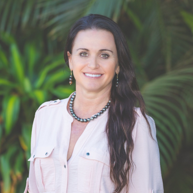 Professional woman with long dark hair smiling, wearing pink blouse and pearl necklace