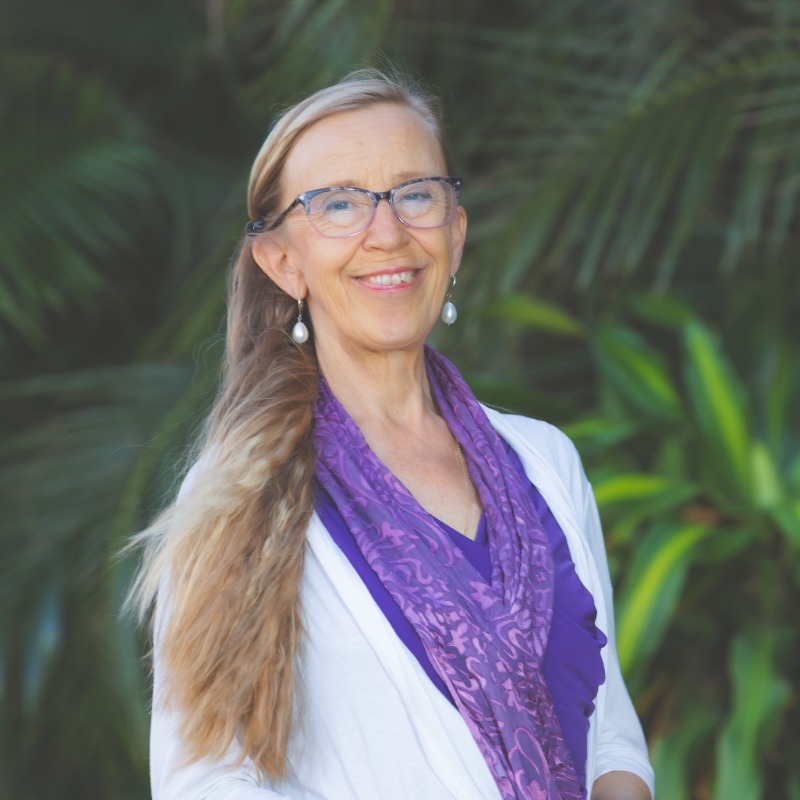 Woman with glasses and long hair smiling in front of green plant background