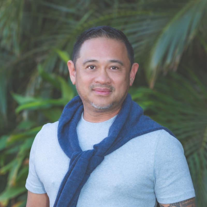 Middle-aged man in light blue shirt and blue scarf with tropical foliage background