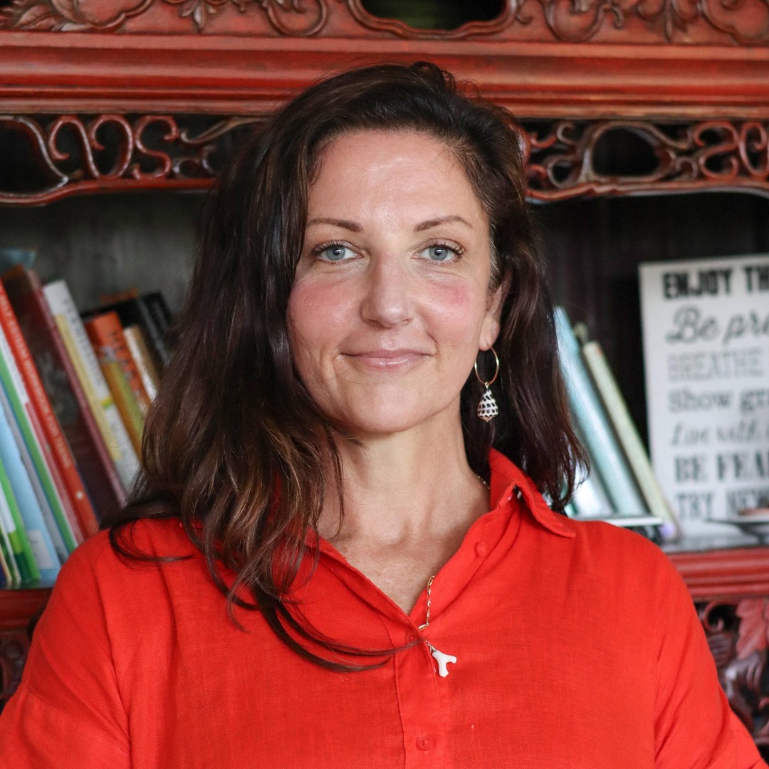 Woman in red shirt smiling in front of ornate red shelving with books