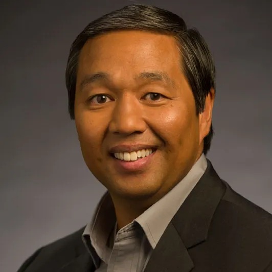 Professional headshot of a smiling middle-aged Asian man in business casual attire.
