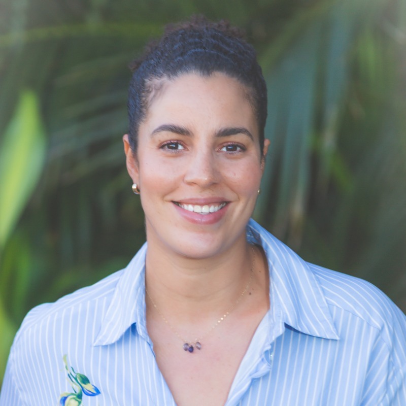 Professional headshot of smiling woman in blue striped shirt with blurred green background