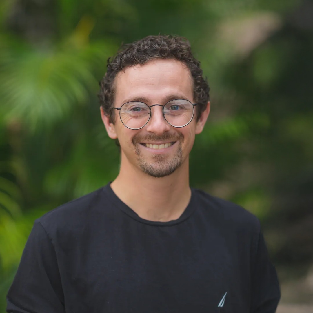 Smiling man with curly hair and glasses wearing black shirt outdoors