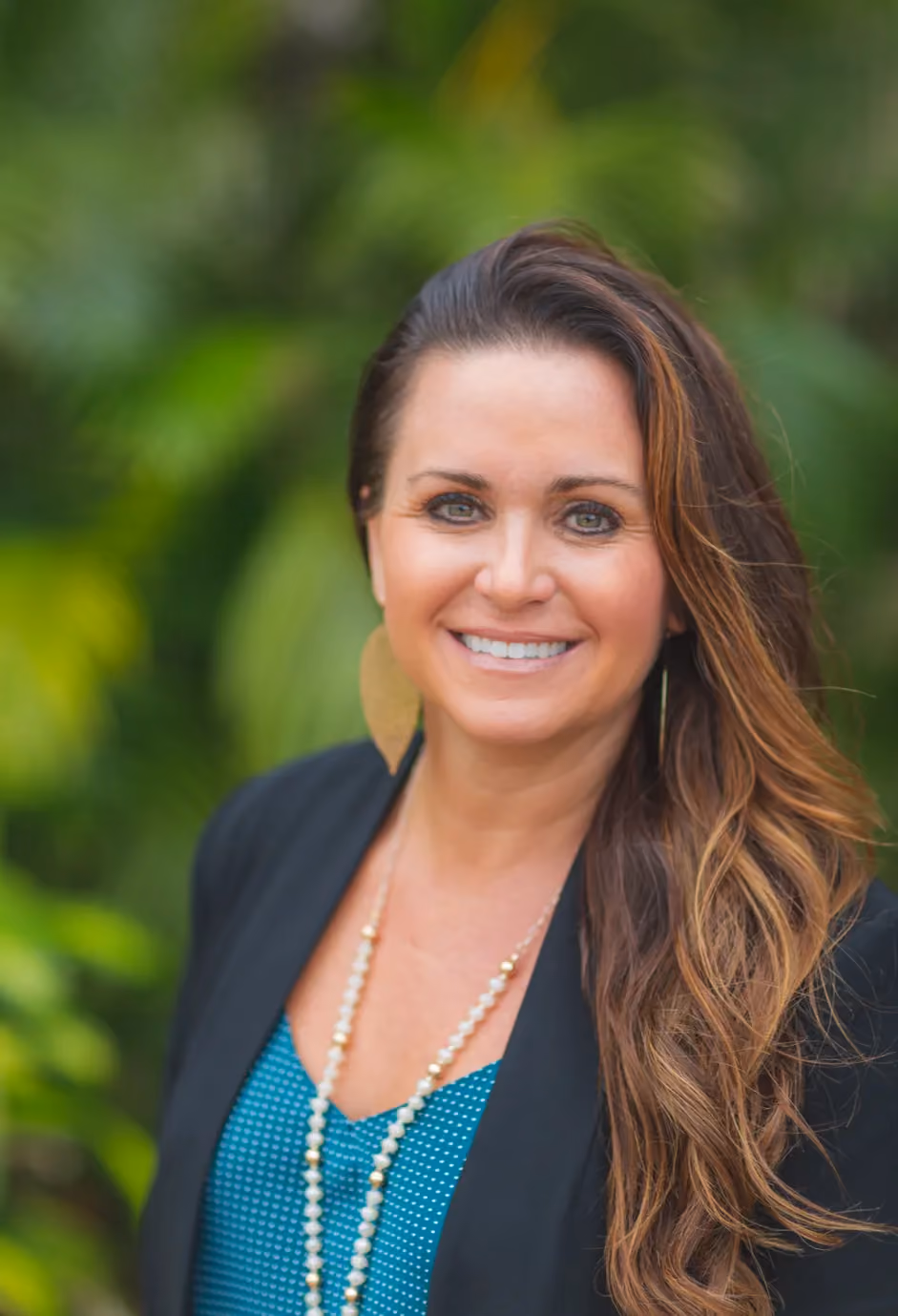 Professional headshot of woman with long brown hair, pearl necklace, blue top, green background