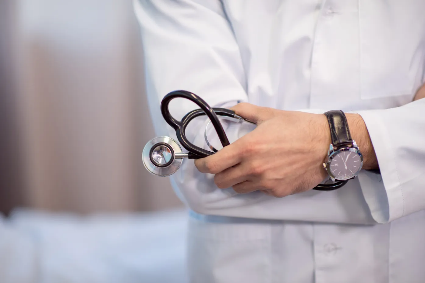 Doctor in white coat holding stethoscope with watch, medical professional portrait