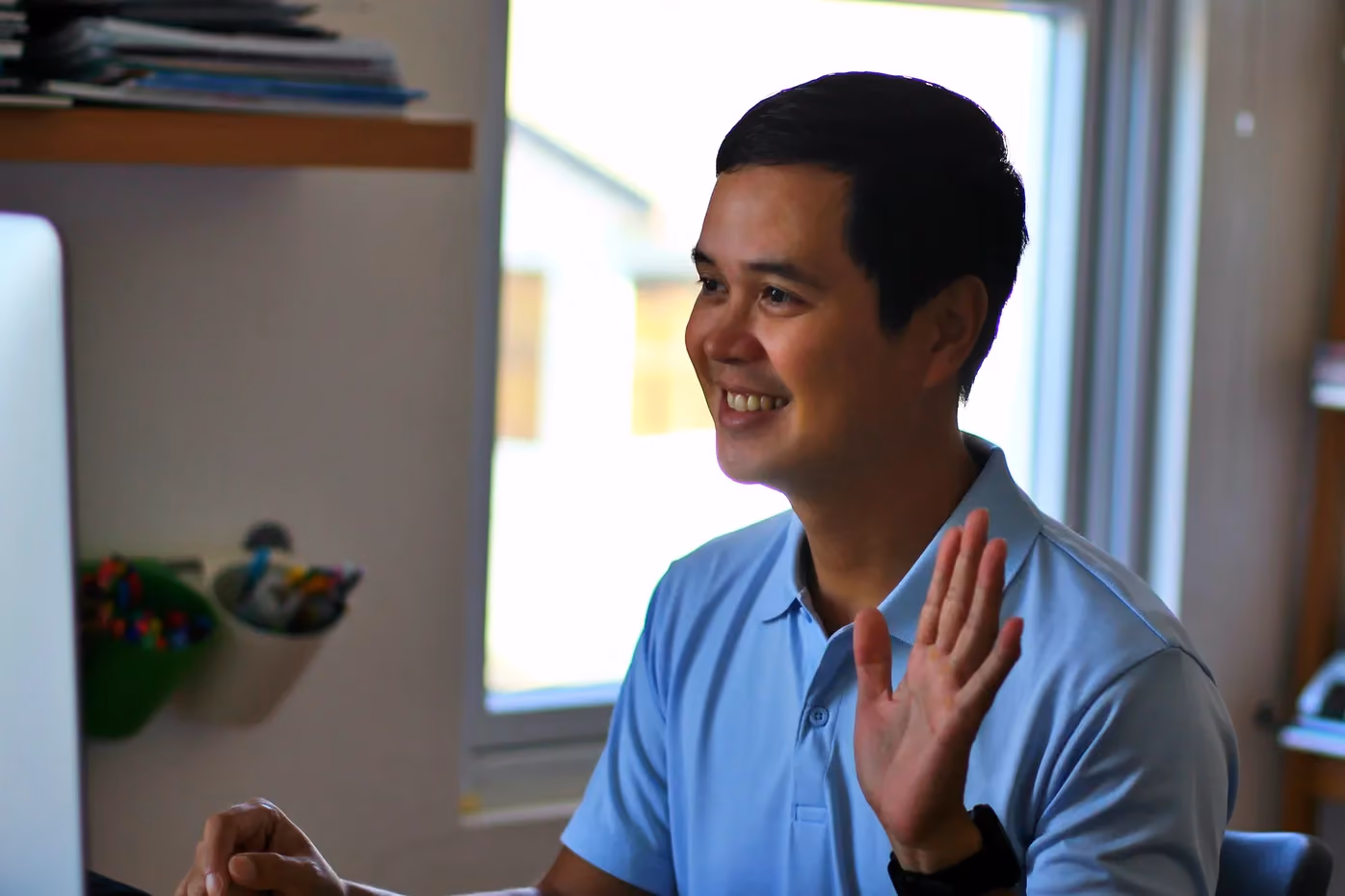 Man in light blue shirt smiling and gesturing with hands in office setting