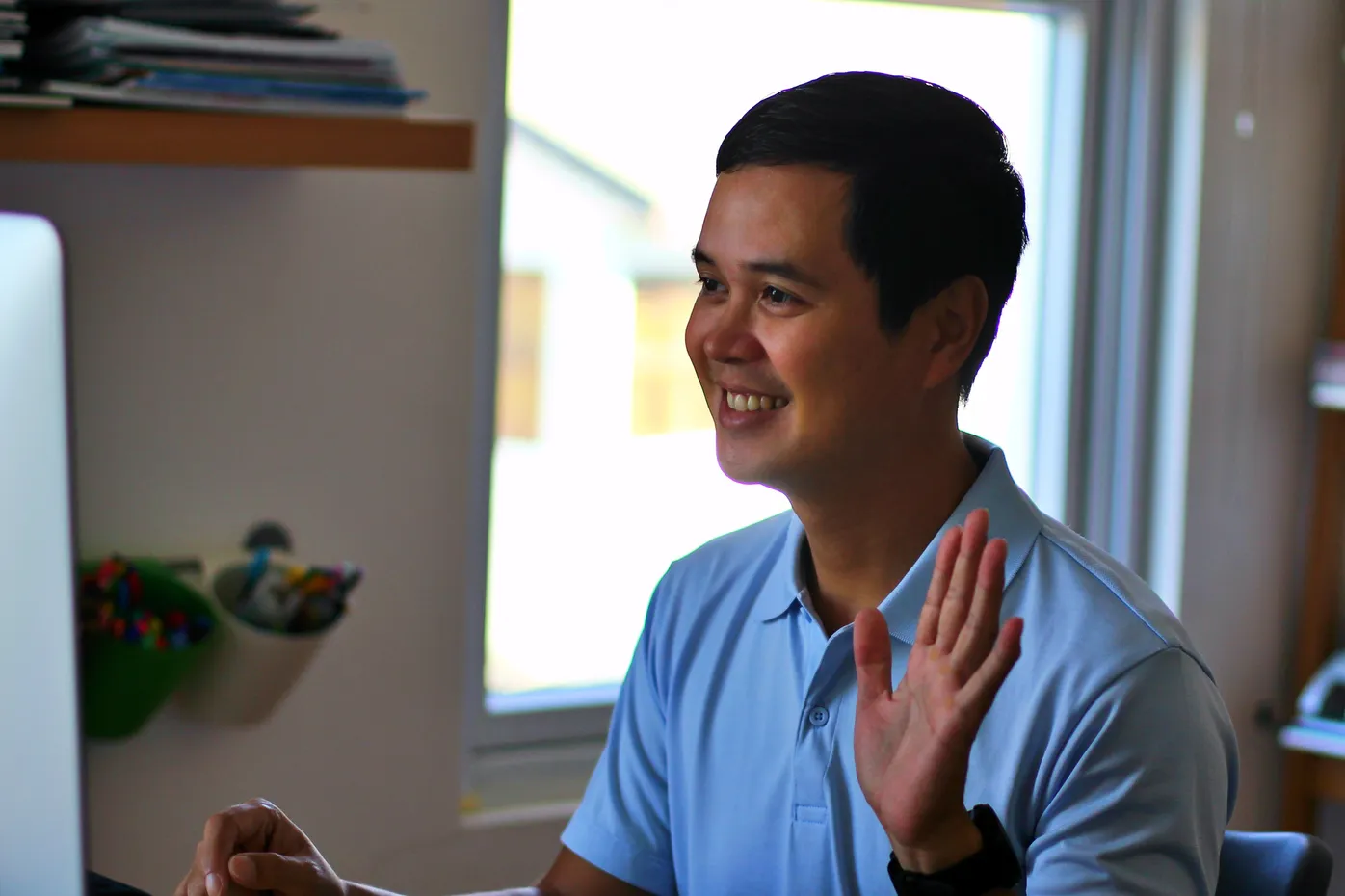 Man in light blue shirt smiling and gesturing with hands in office setting