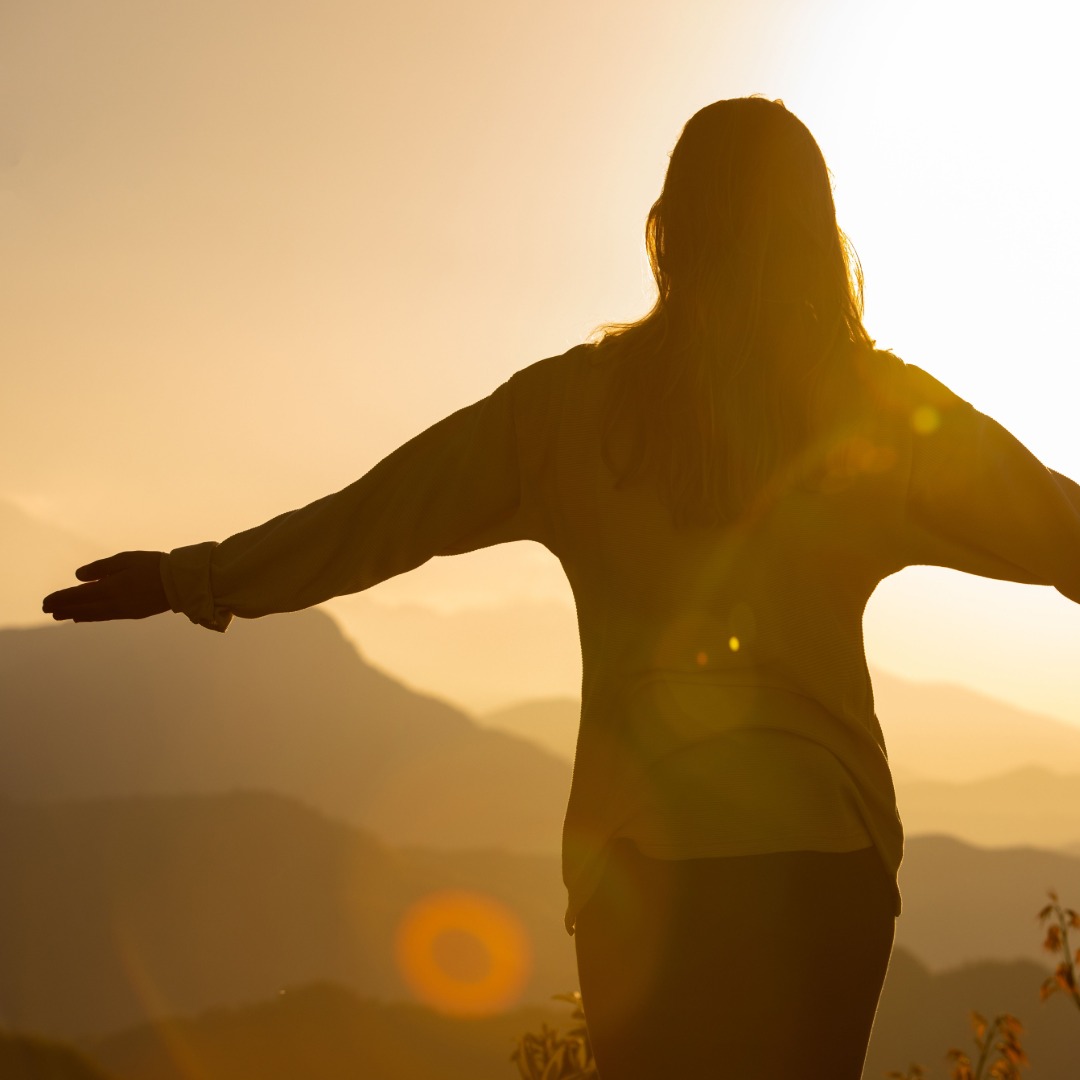 Silhouette of woman with arms outstretched at golden sunset over mountains