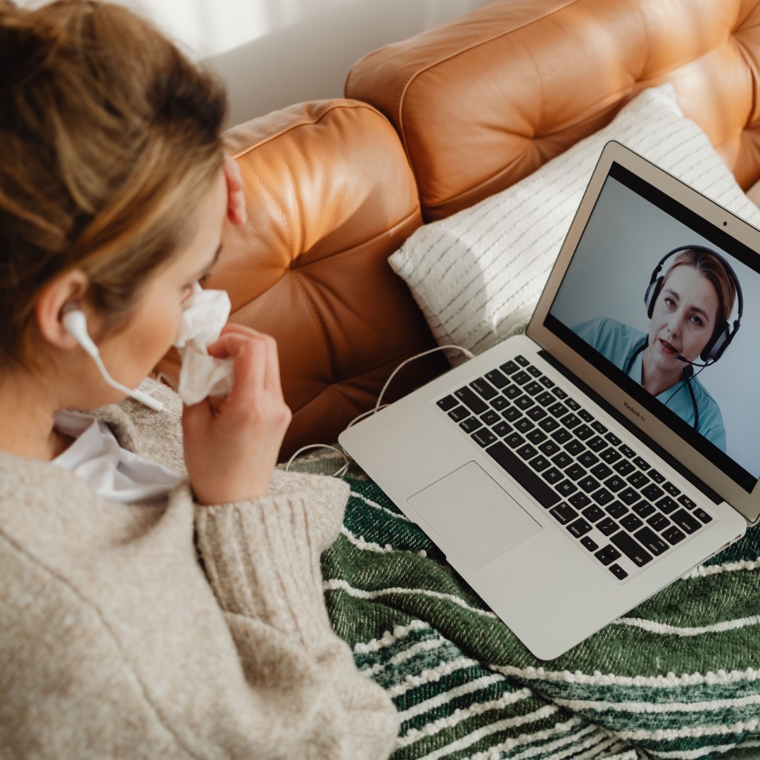 Child in headphones video calling with woman on laptop, seated on brown couch.