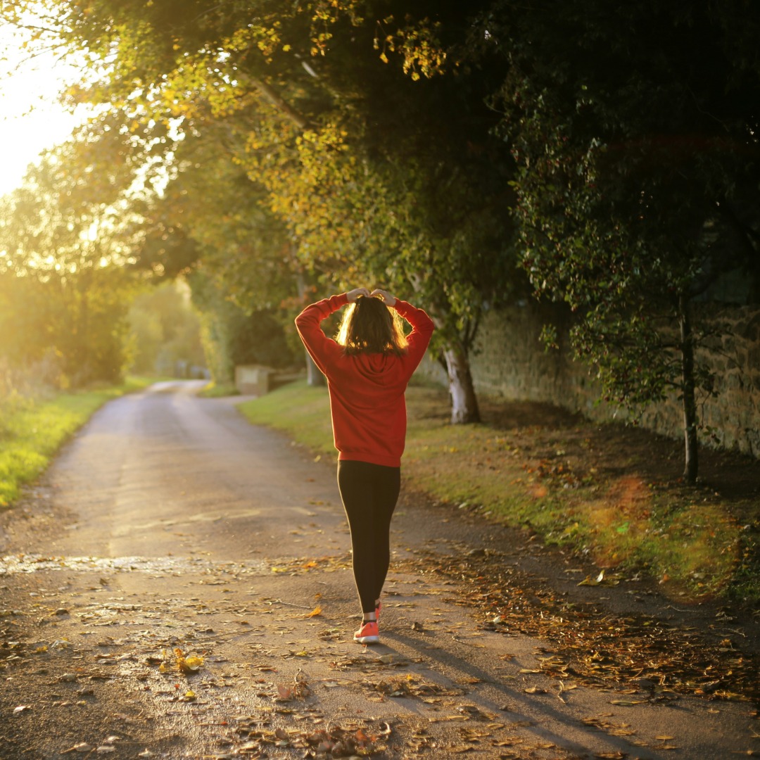Woman jogging on tree-lined path during golden sunset with arms raised