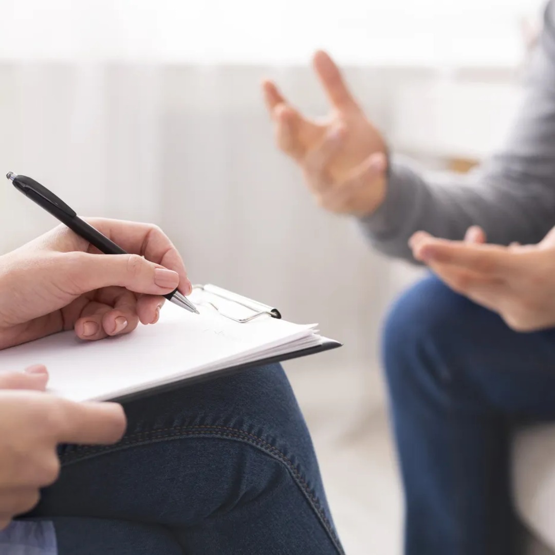 Person holding clipboard with pen, taking notes during conversation with another person