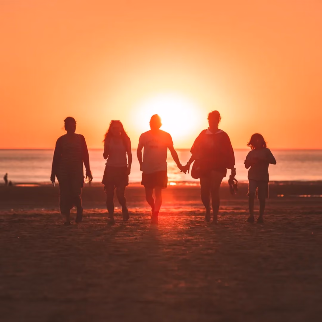 Silhouettes of five people holding hands on beach at sunset.