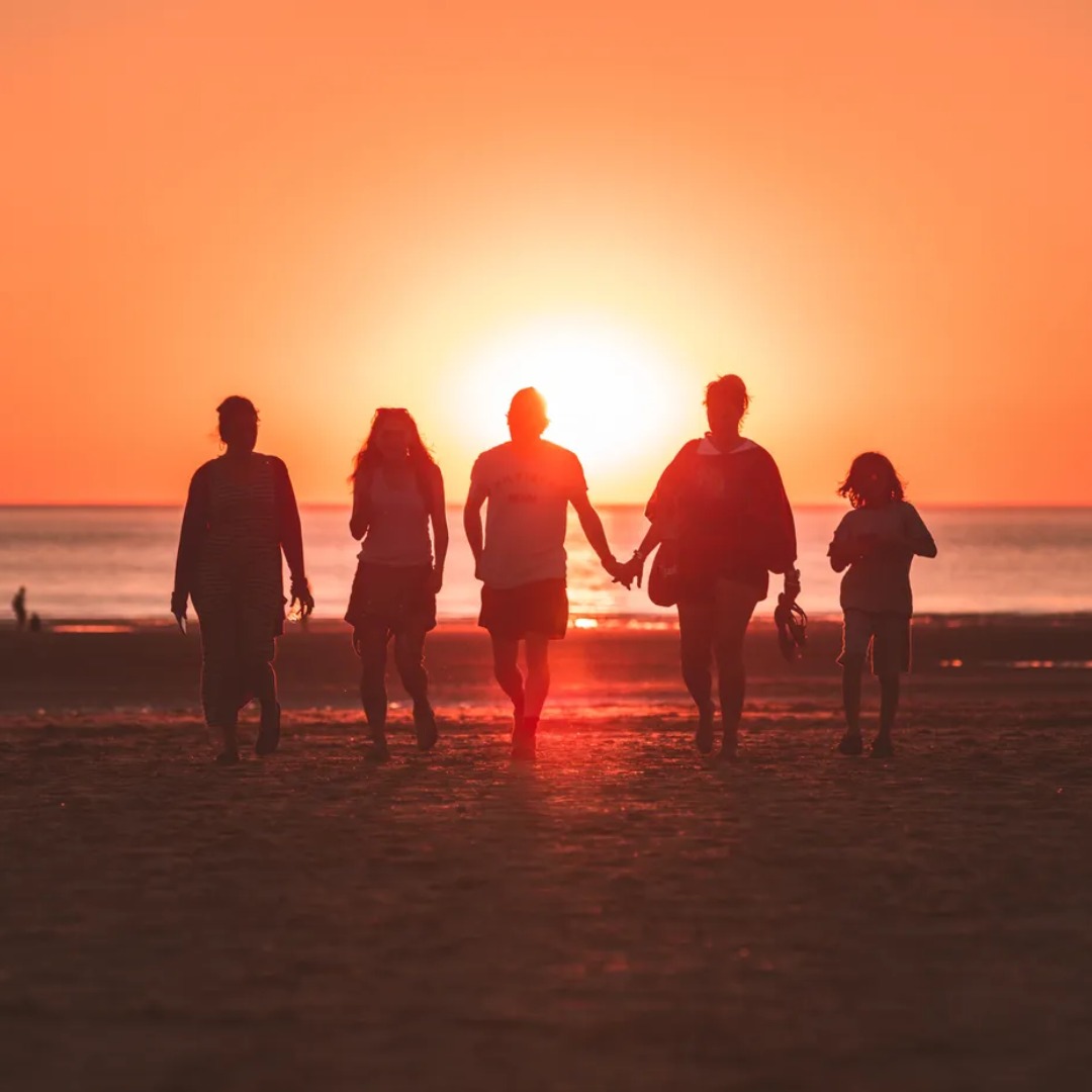 Silhouettes of five people holding hands on beach at sunset.
