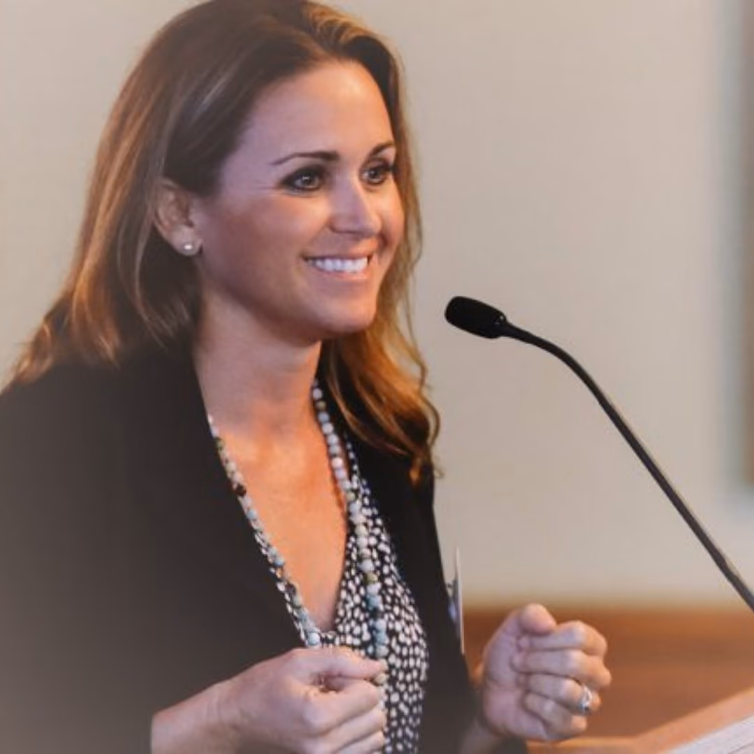Woman with auburn hair smiling at microphone during professional presentation