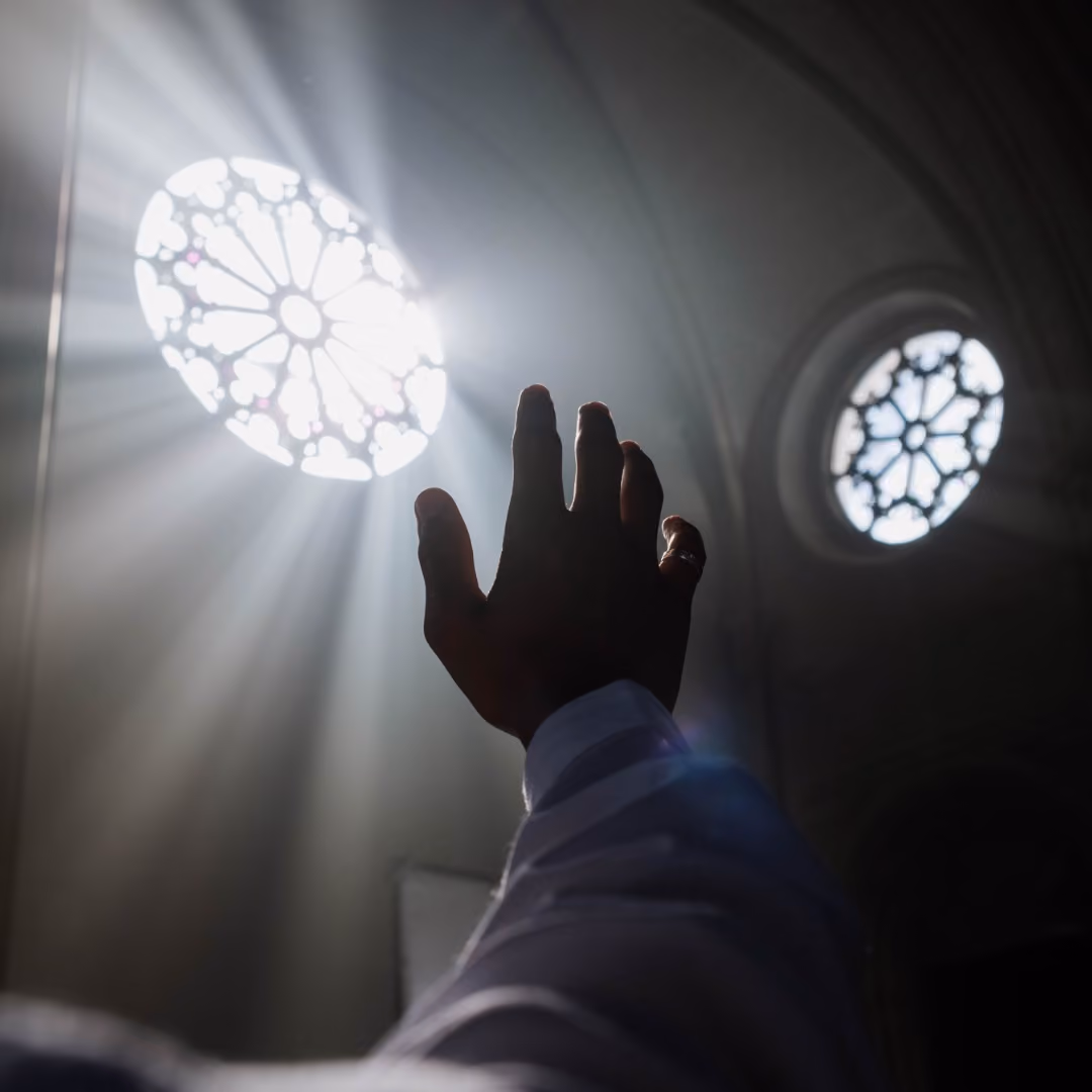 Silhouetted hand reaching toward bright ornate rose windows in Gothic cathedral