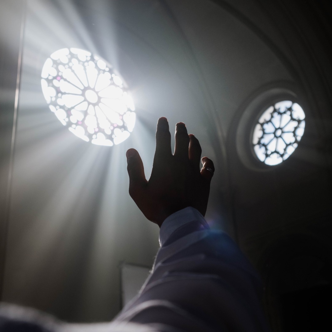 Silhouetted hand reaching toward bright ornate rose windows in Gothic cathedral