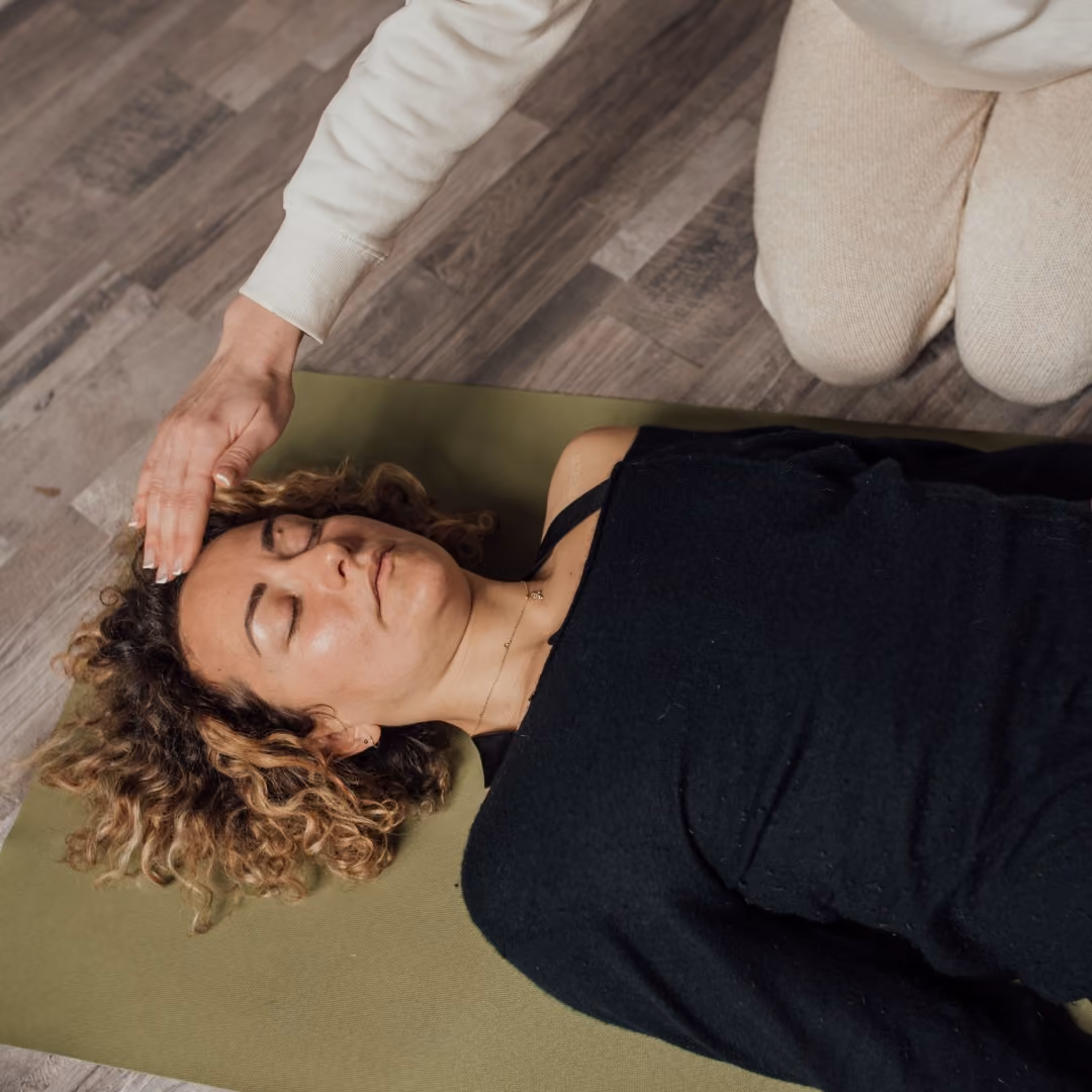 Woman with curly hair lying on yoga mat receiving head massage from caregiver