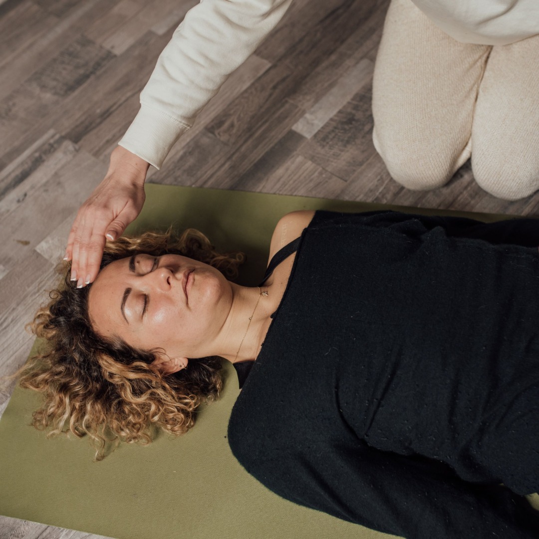 Woman with curly hair lying on yoga mat receiving head massage from caregiver