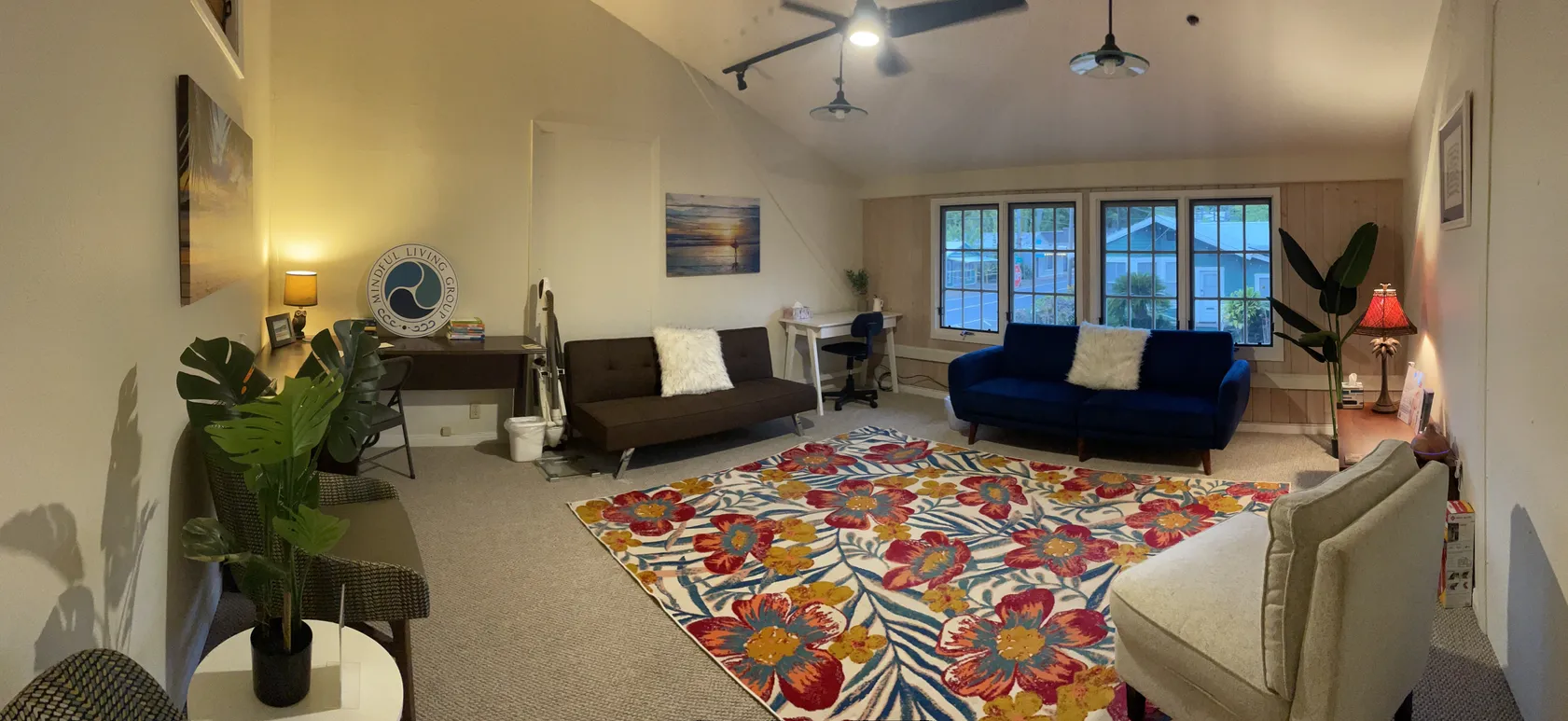 Modern living room with colorful floral rug, multiple sofas, plants, and large windows overlooking mountains
