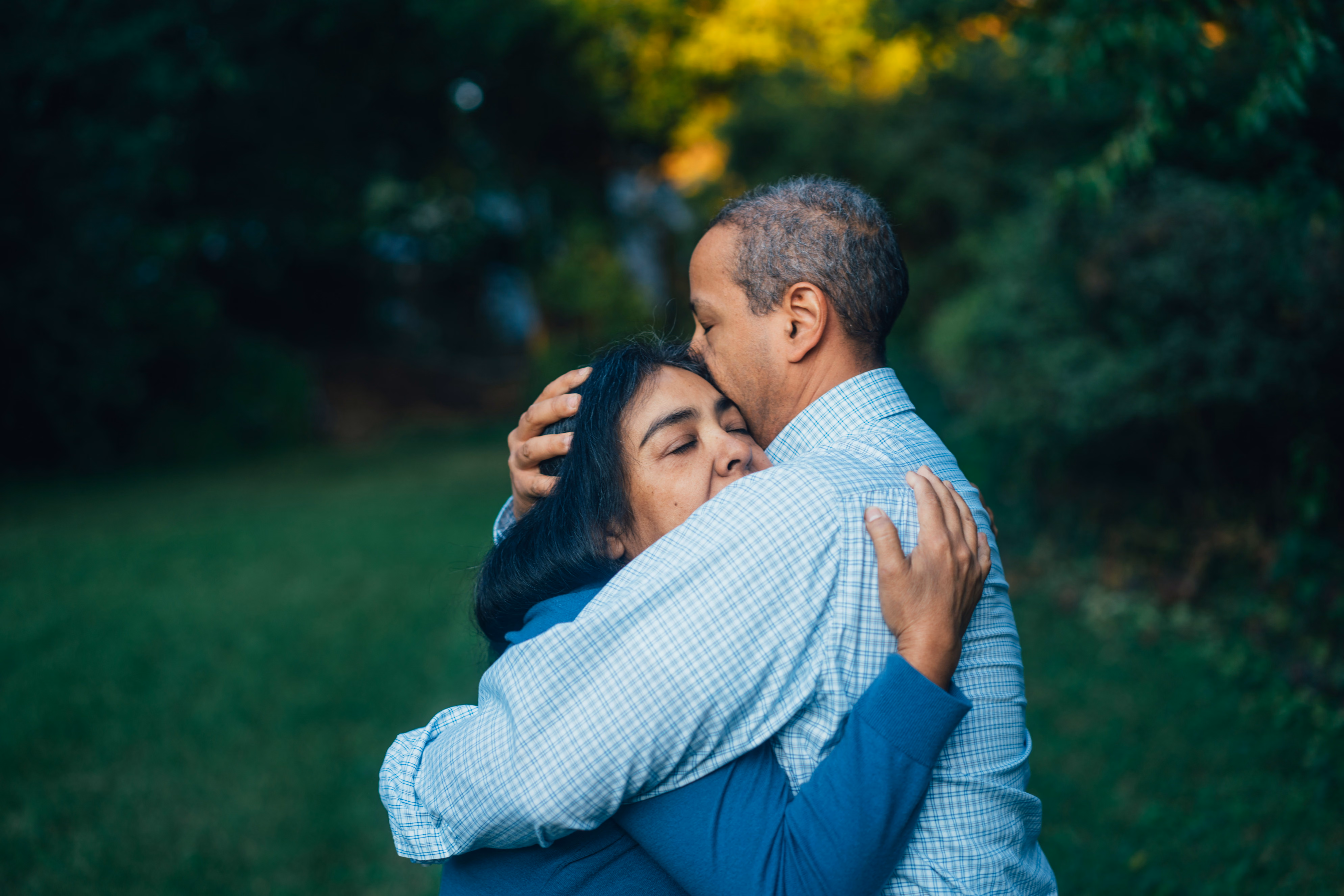 Man and woman embracing outdoors in front of green garden and trees