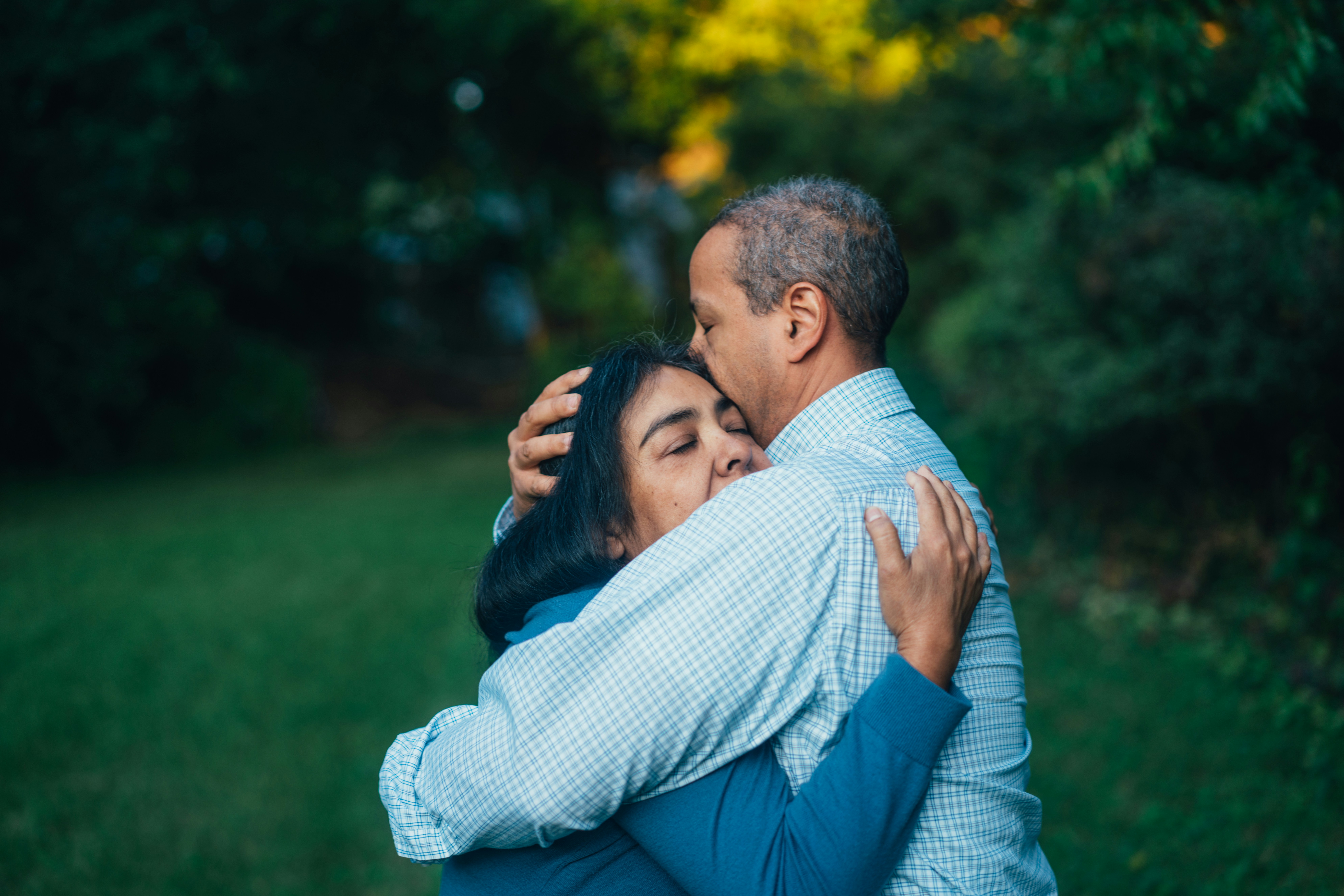 Man and woman embracing outdoors in front of green garden and trees