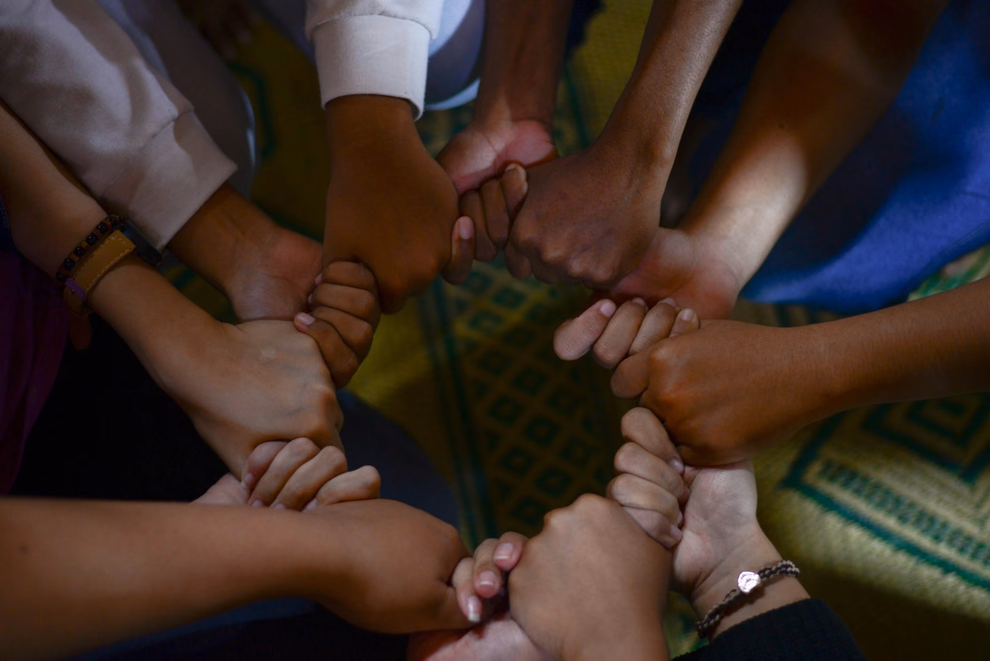 Diverse group of people joining hands together in a circle, showing unity and teamwork.