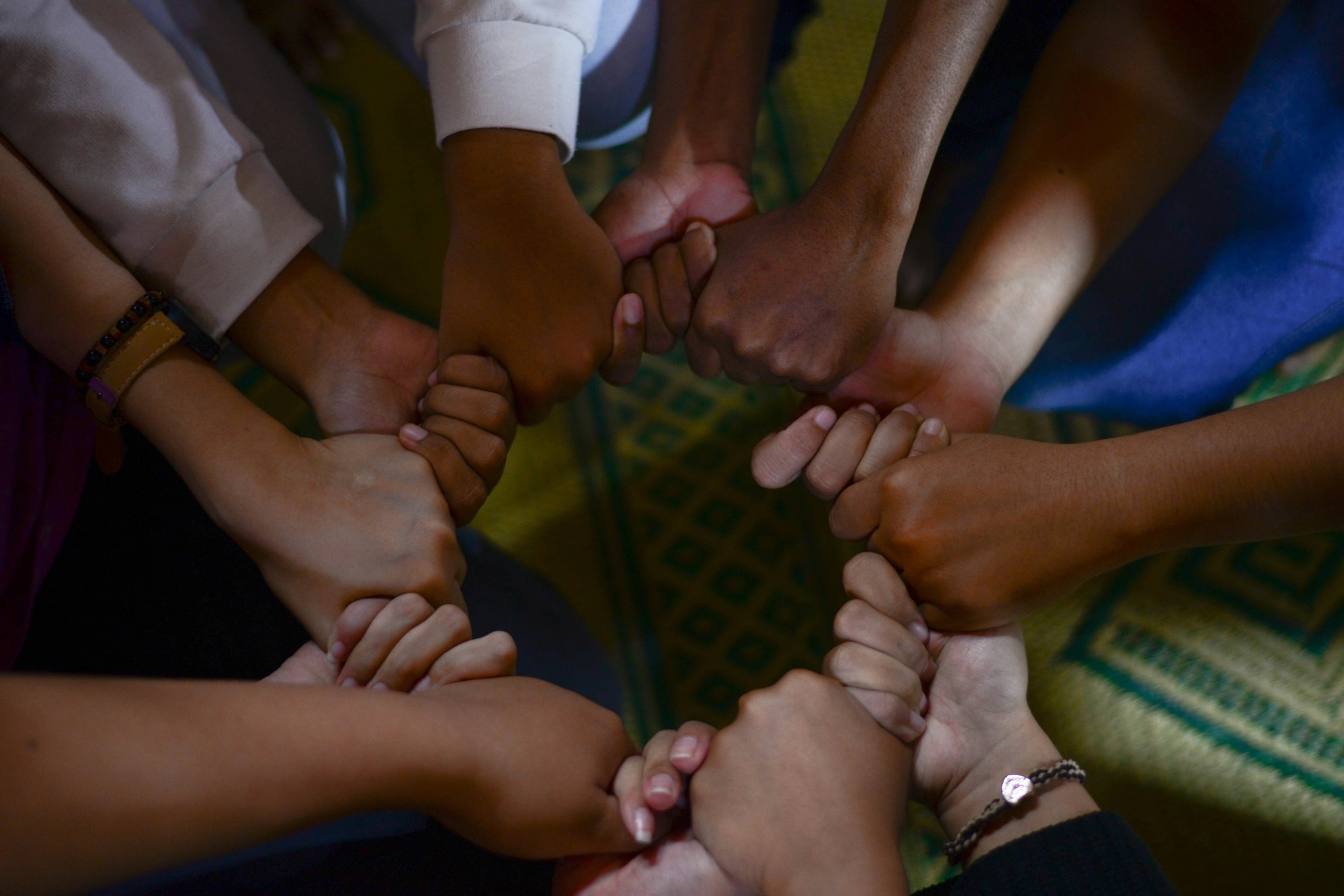 Diverse group of people joining hands together in a circle, showing unity and teamwork.
