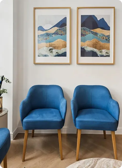 Two blue armchairs beneath framed landscape prints in a practice waiting area