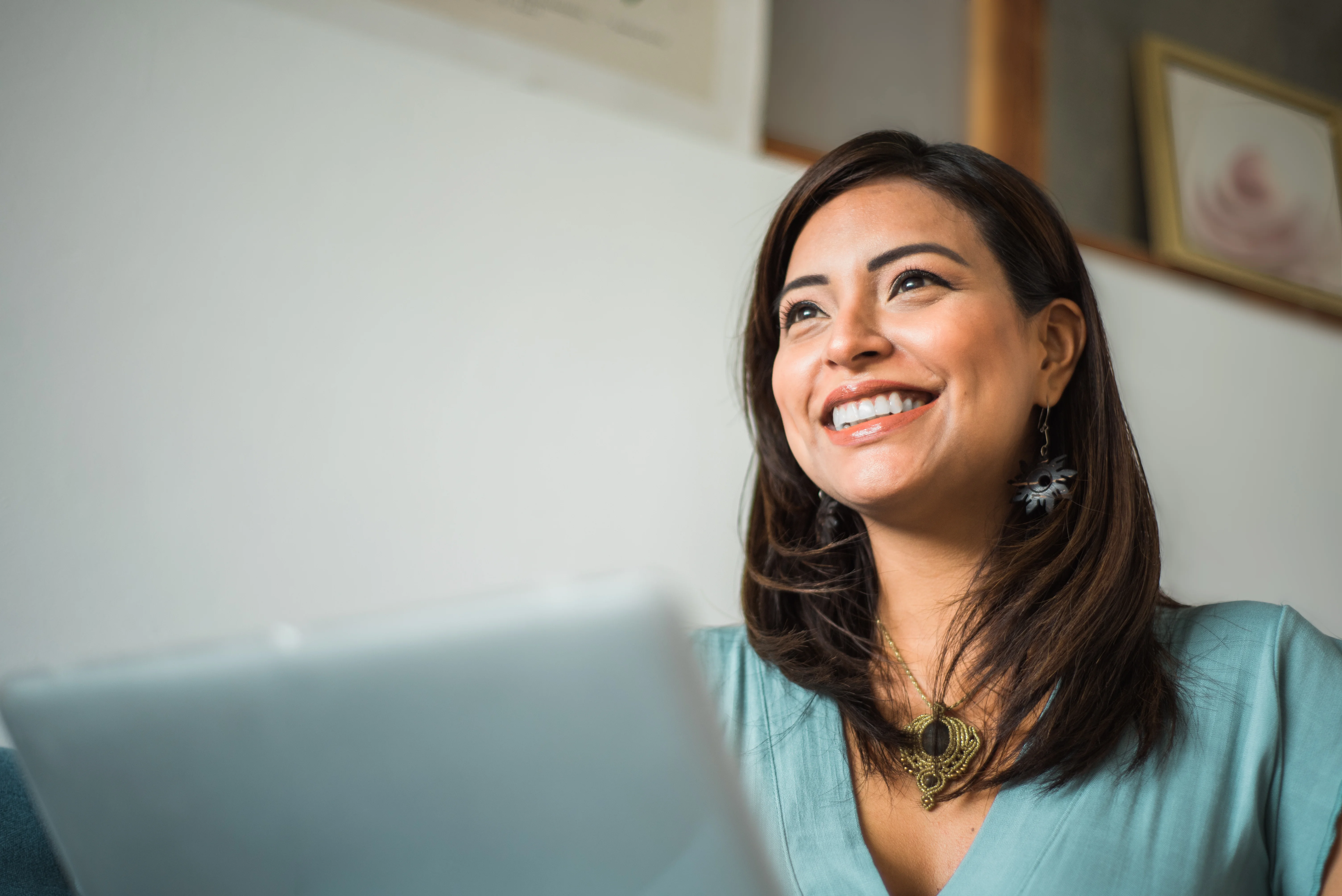 Smiling woman looking upwards beside a laptop in a bright room